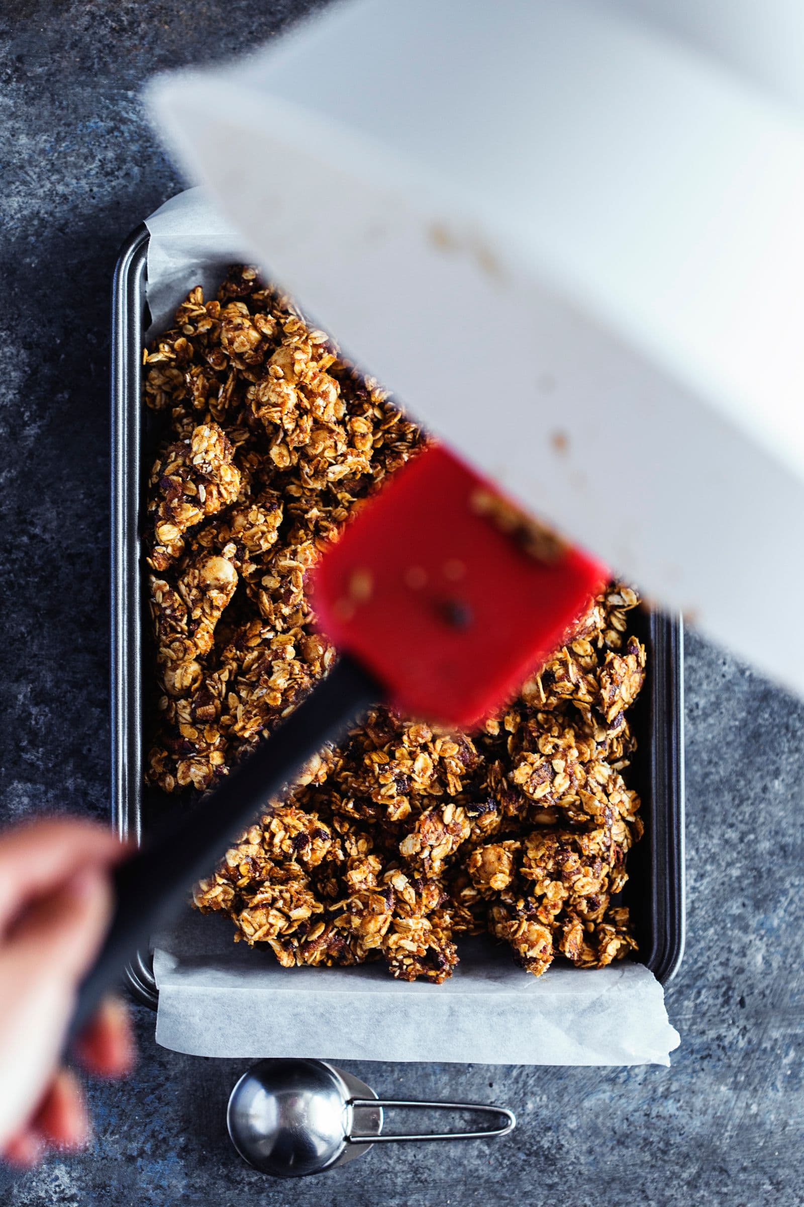 Scooping and spreading granola dough into a lined baking tin.