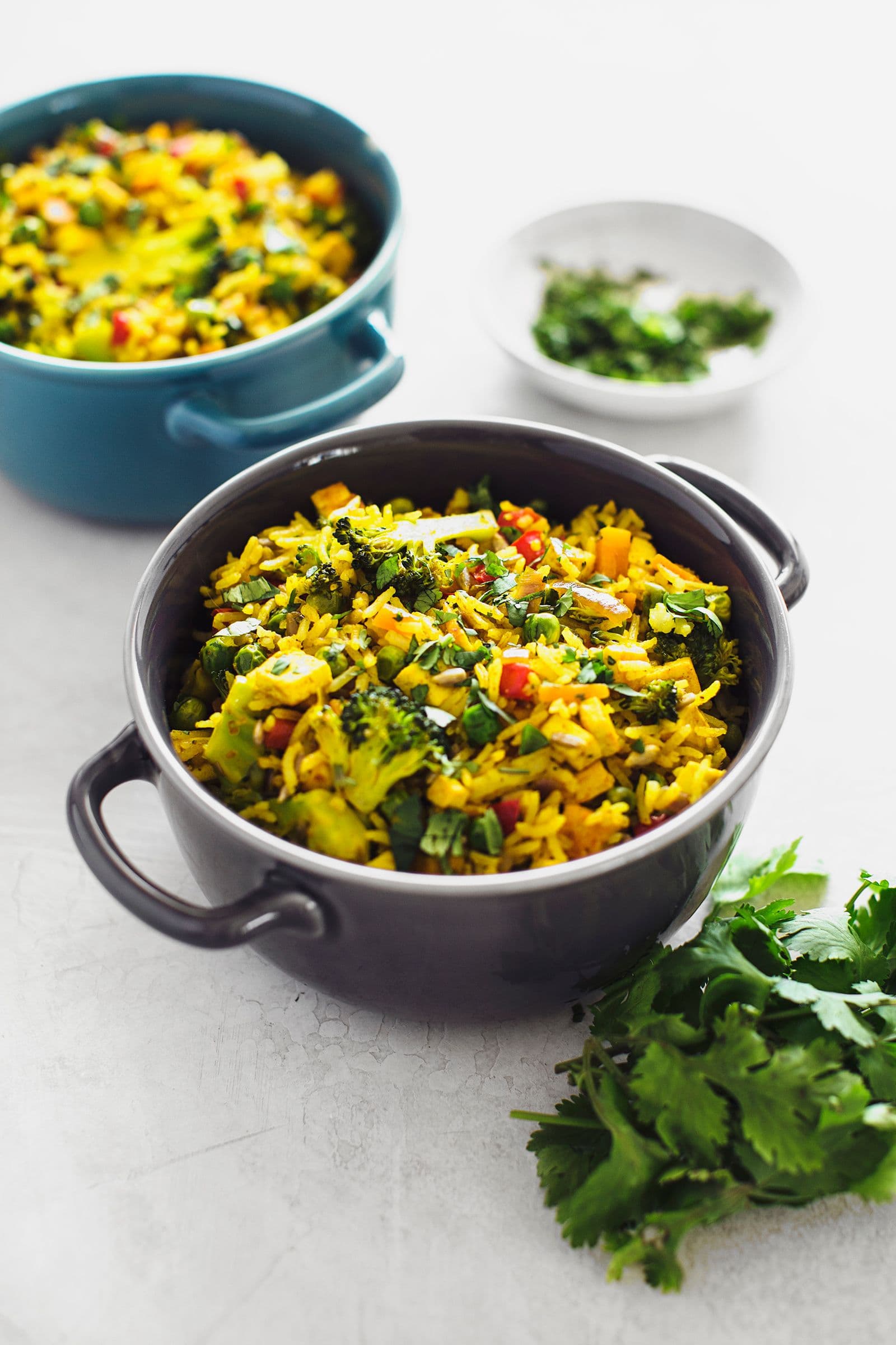 Two bowls filled with vegan fried rice and fresh coriander on a white background.