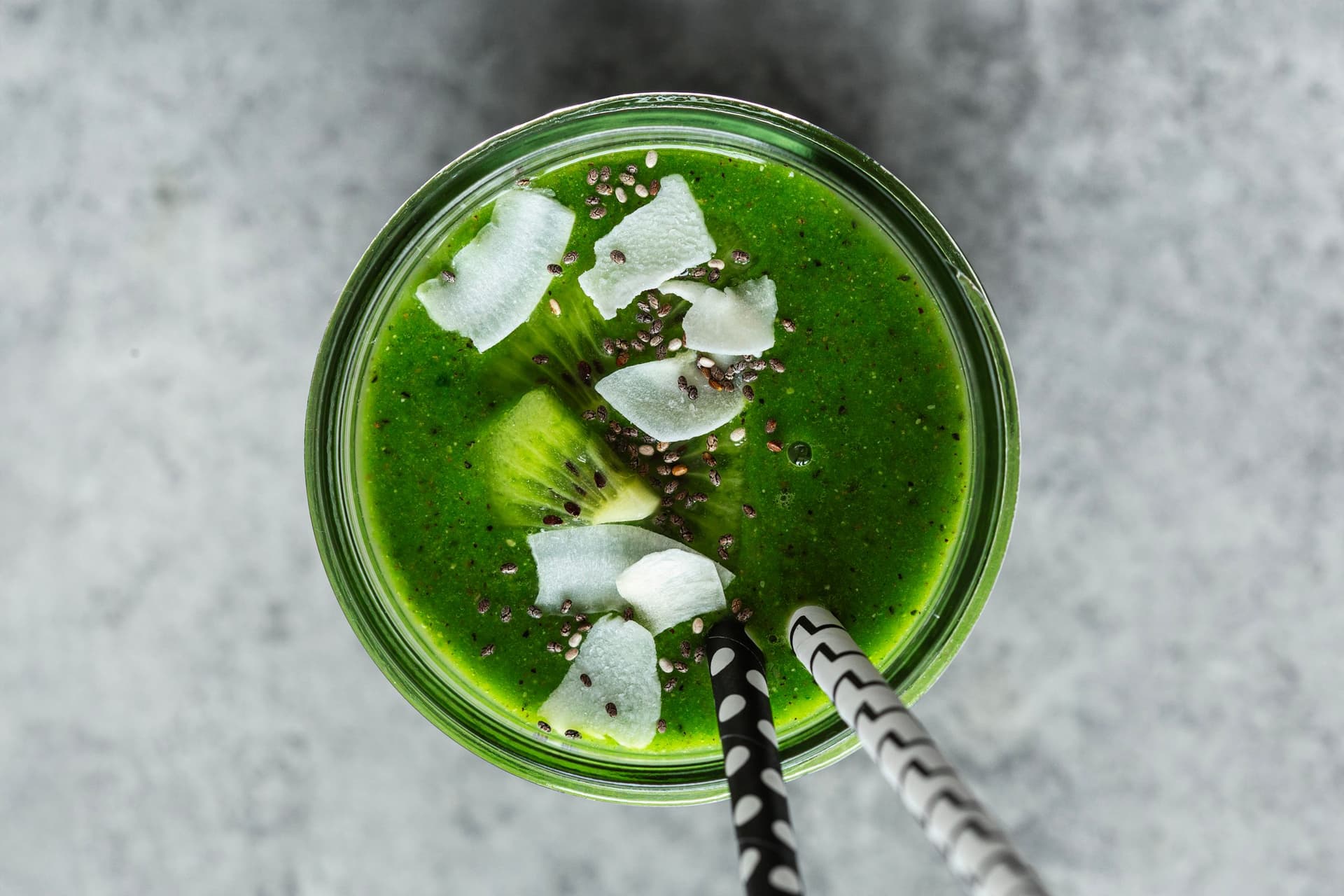 Vibrant green smoothie in a glass jar topped with kiwi, coconut flakes, and chia seeds