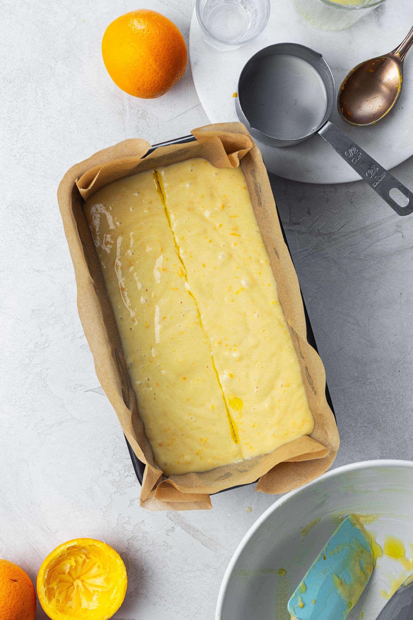 Loaf pan lined with parchment paper filled with orange cake batter, scored down the center with an oil-coated knife.