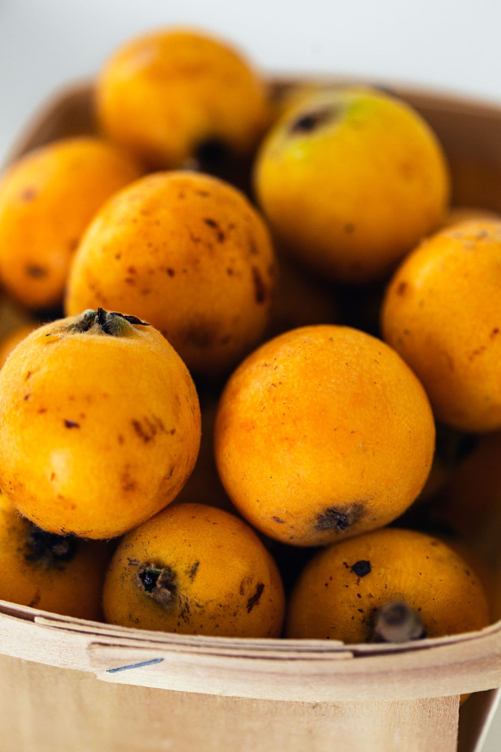 Fresh loquats with golden skin and dark speckles, piled in a small wooden basket, photographed up close