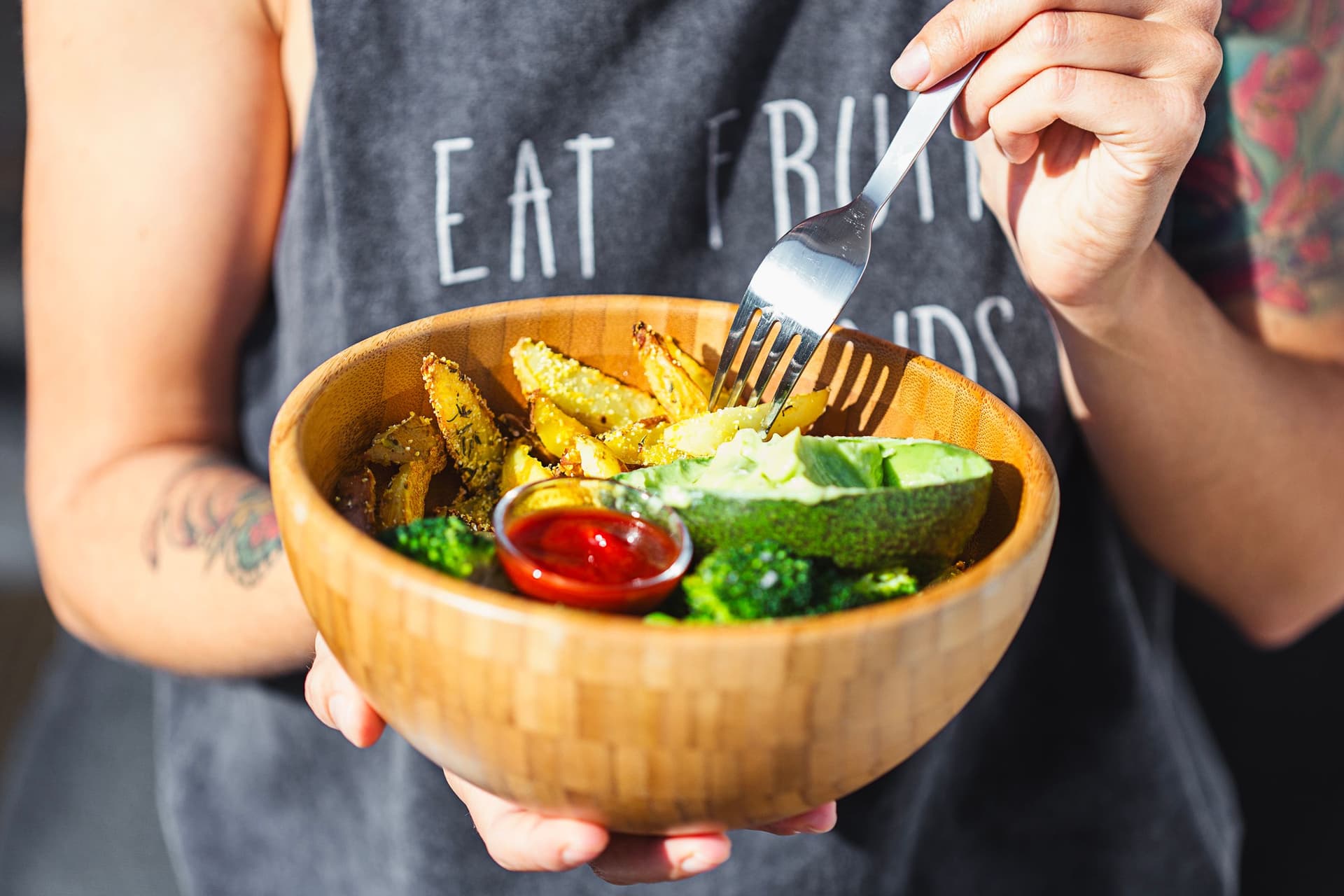 Person holding a bowl of crispy baked wedges, broccoli and dips, about to eat.