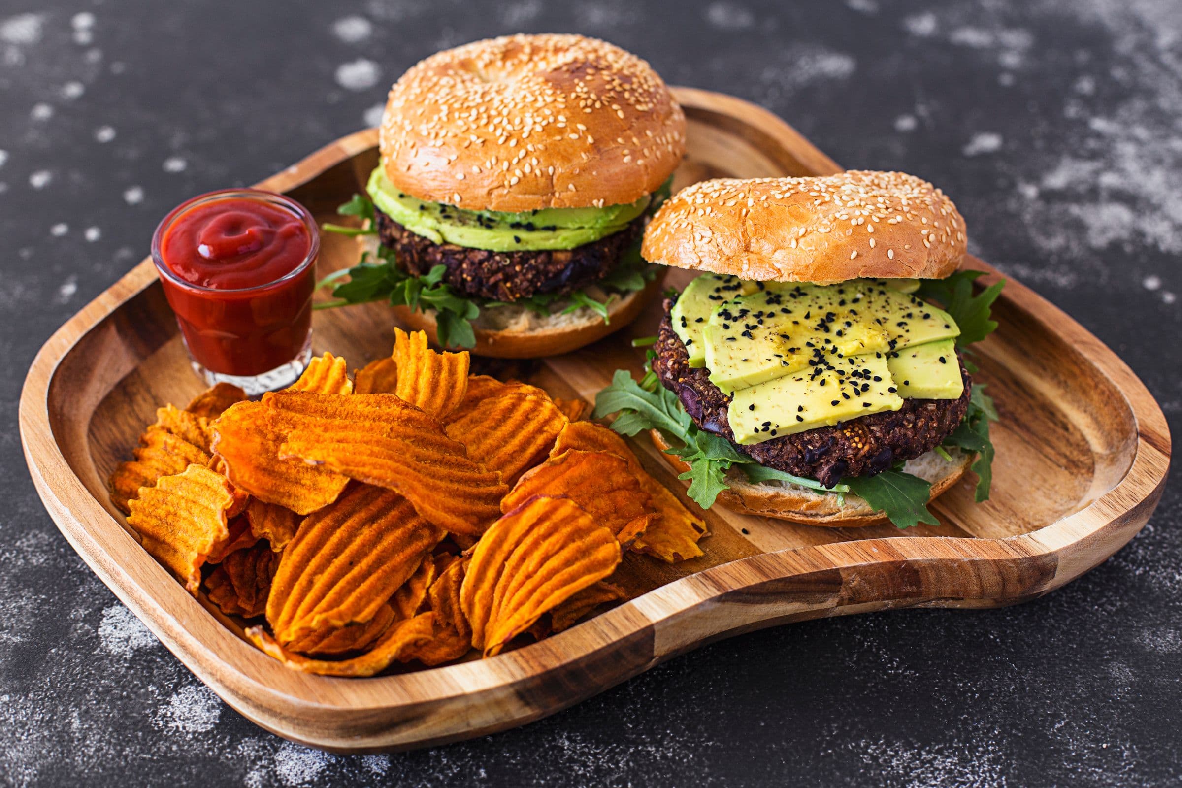 Two black bean burgers served with sweet potato chips and ketchup.