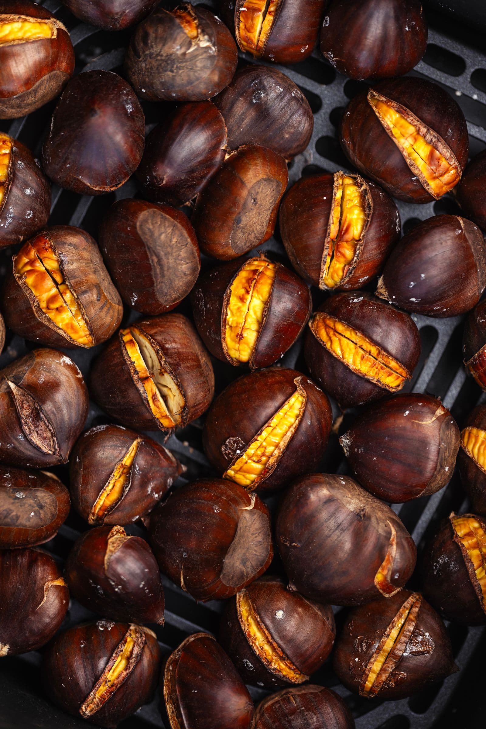 Close-up of roasted chestnuts inside the air fryer, showing the bright yellow flesh peeking through the opened shells.