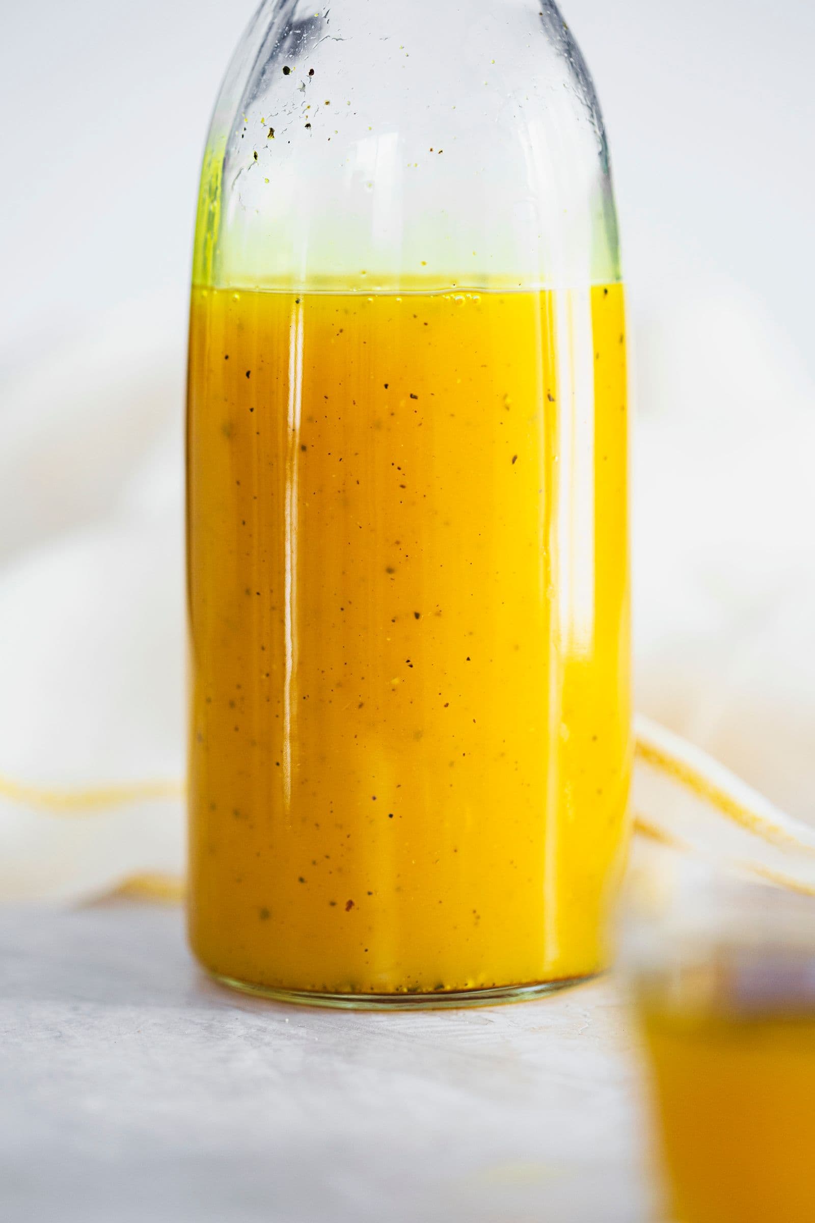 Xarope caseiro de gengibre e curcuma numa garrafa de vidro alta, com pintinhas de pimenta.