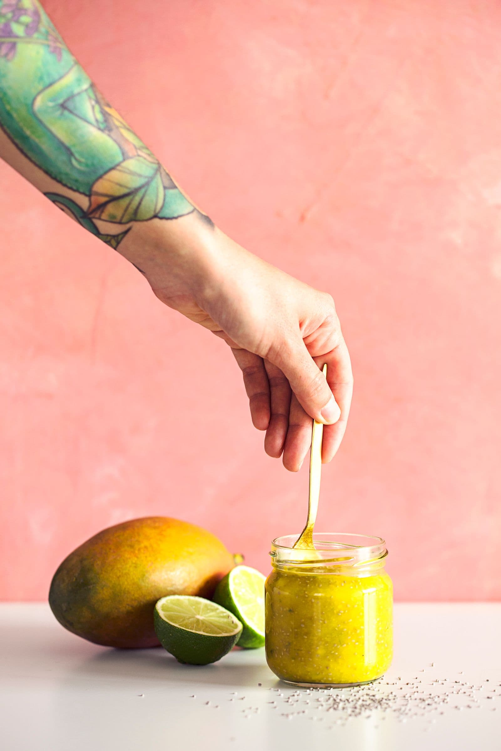 Hand holding spoon over a small glass jar with fresh mango chia jam.