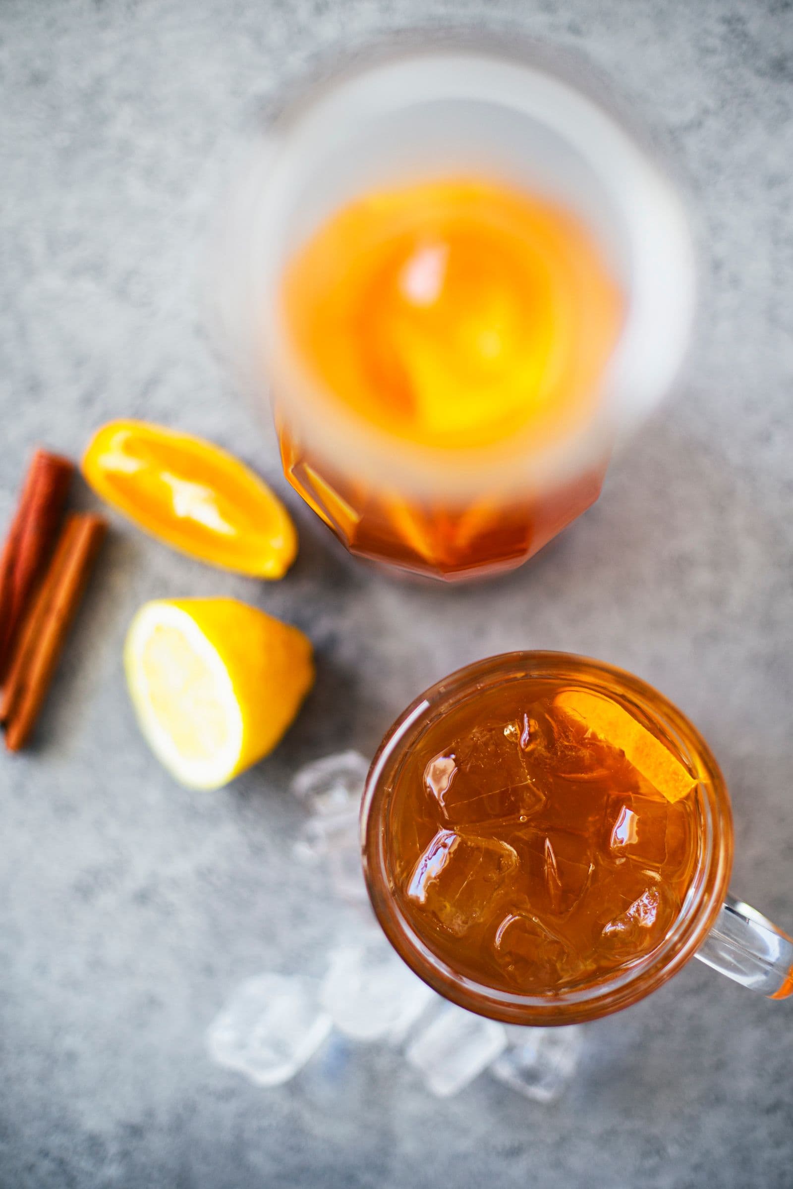 Overhead view of iced tea in a glass and carafe with citrus slices, cinnamon sticks and ice.
