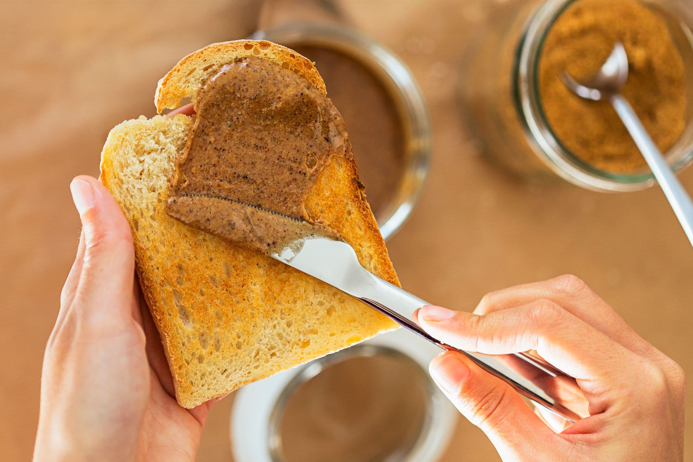 Hands spreading almond butter onto a slice of toast.