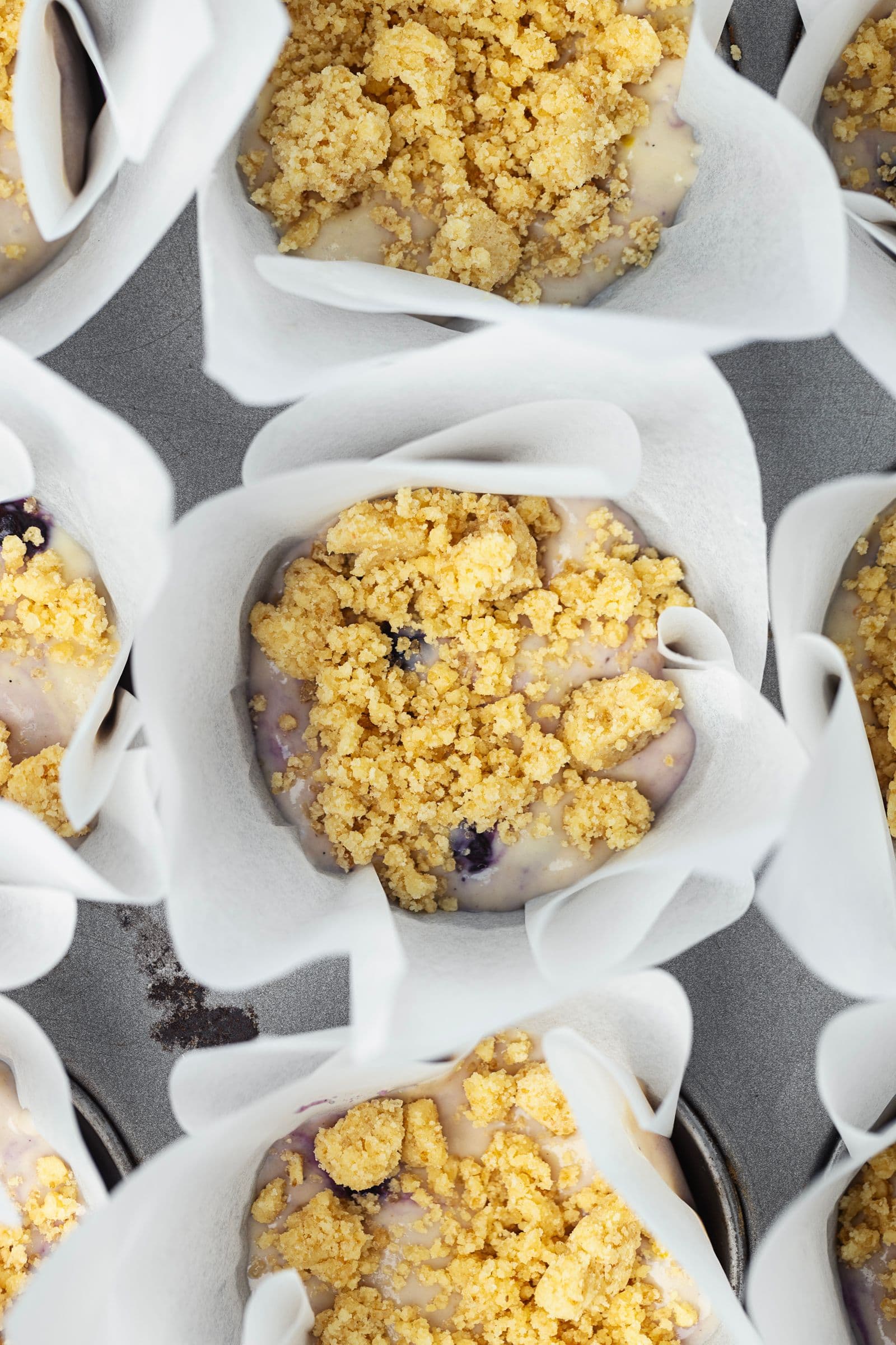 Queques de limão e mirtilos crus, cobertos com crumble, prontos para ir ao forno.