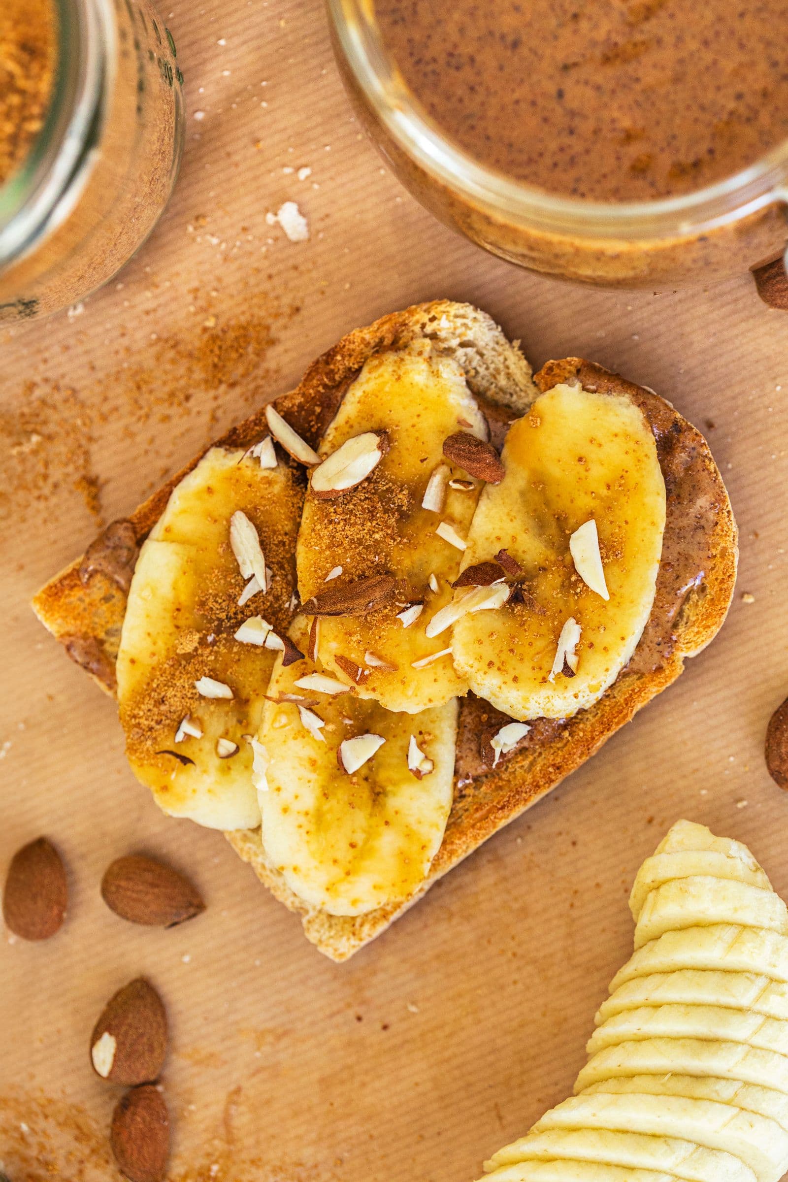 Overhead view of slice of toast topped with almond butter, banana and chopped almonds.
