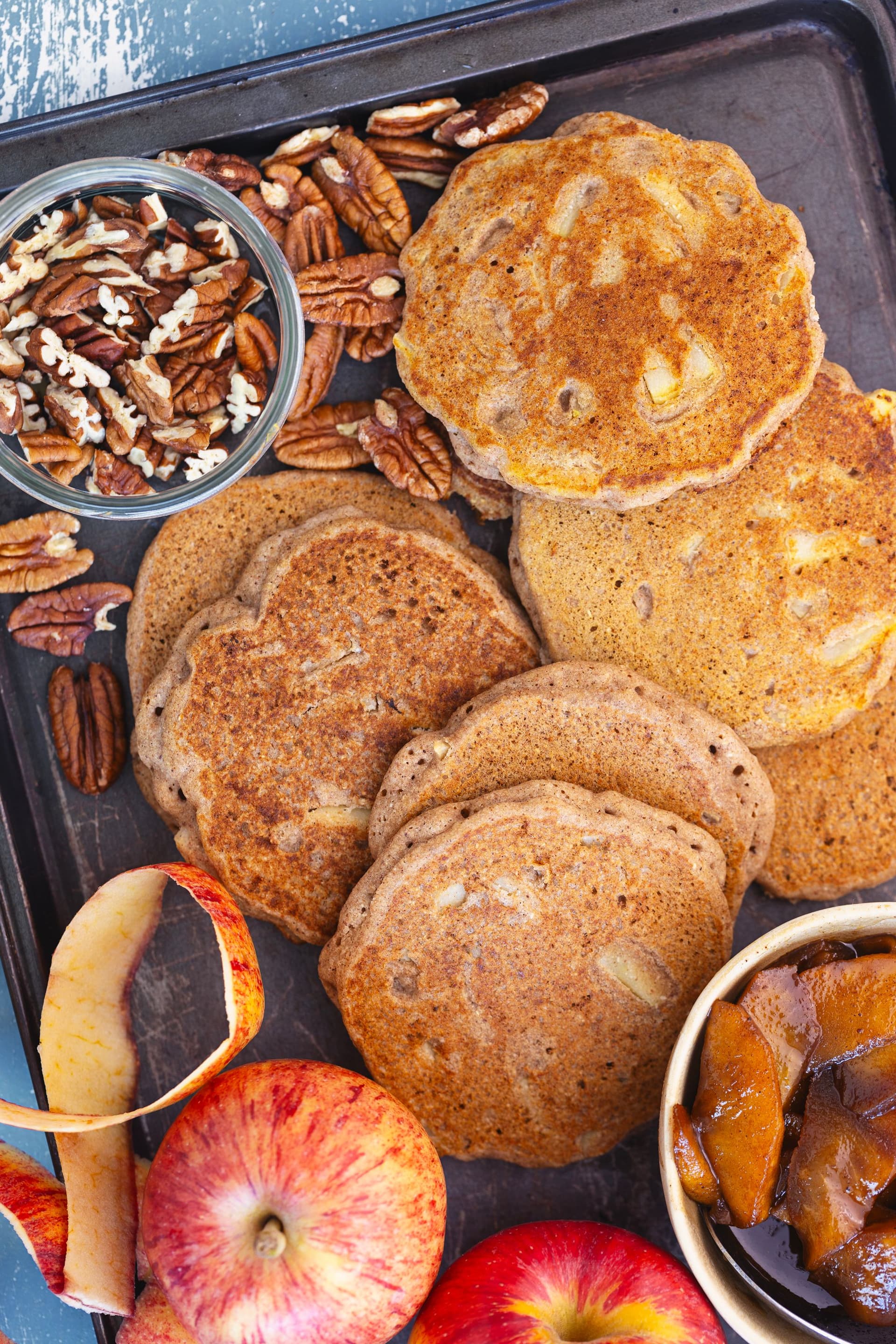 Tabuleiro com panquecas cozinhadas, pecãs, maçãs caramelizadas e maçãs frescas.