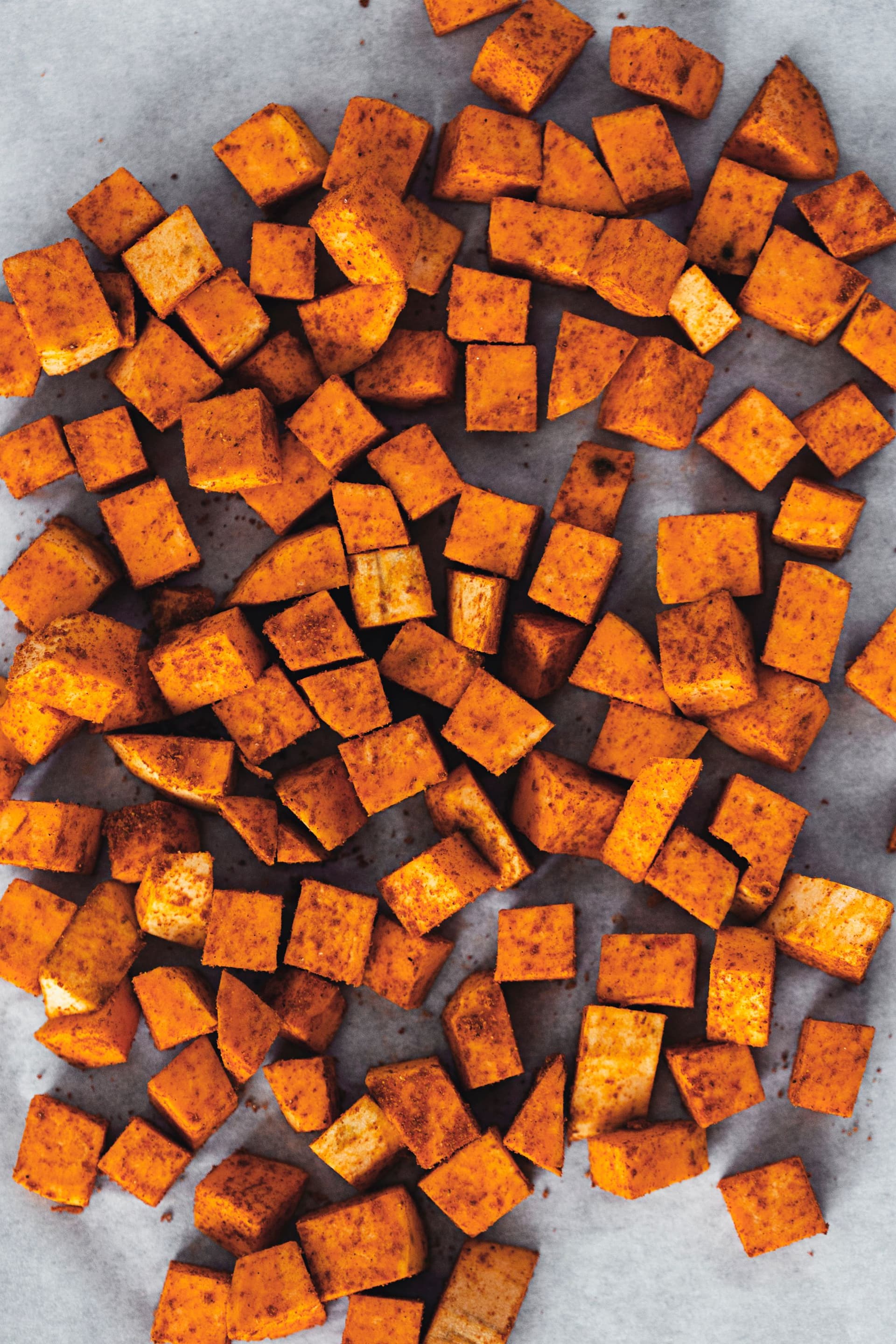 Spiced sweet potato cubes spread on a surface, ready for roasting.