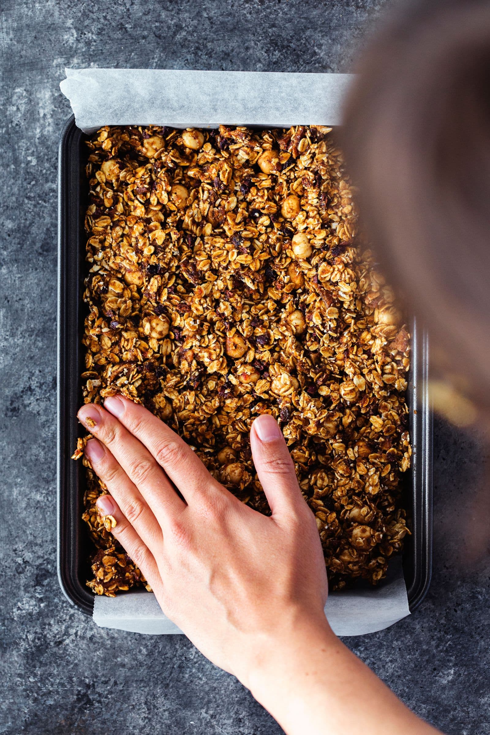 Pressing granola mix evenly into baking tin with hands.