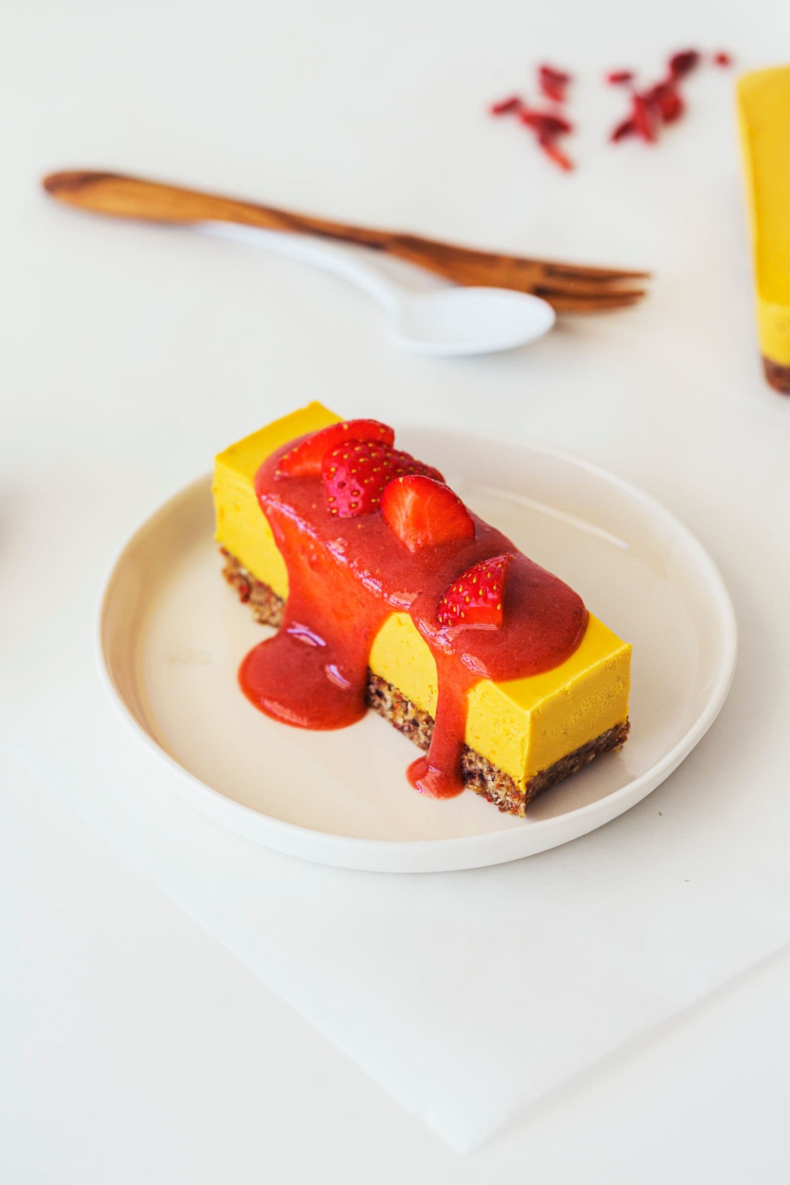 Slice of orange, goji, and strawberry raw vegan cheesecake topped with fresh strawberries and sauce.