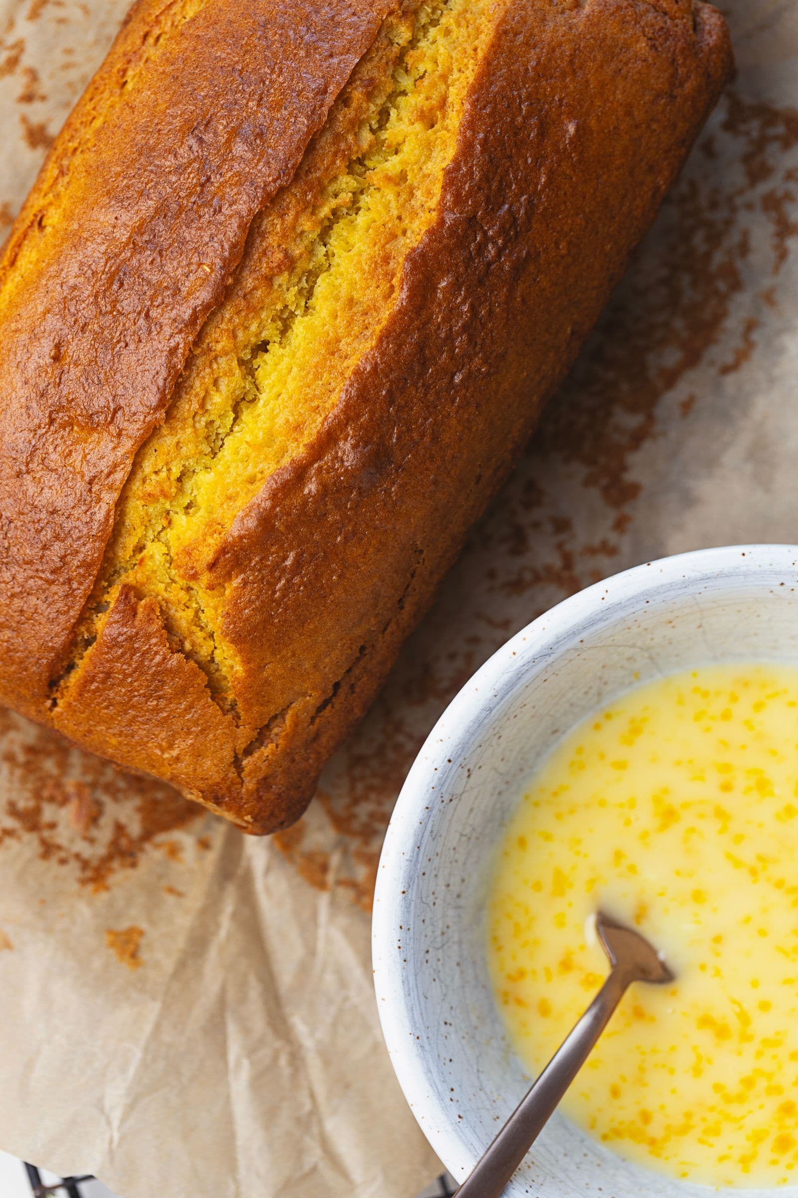 Bolo de laranja acabado de cozer ao lado de uma taça com calda de laranja, pronto a ser glaceado.