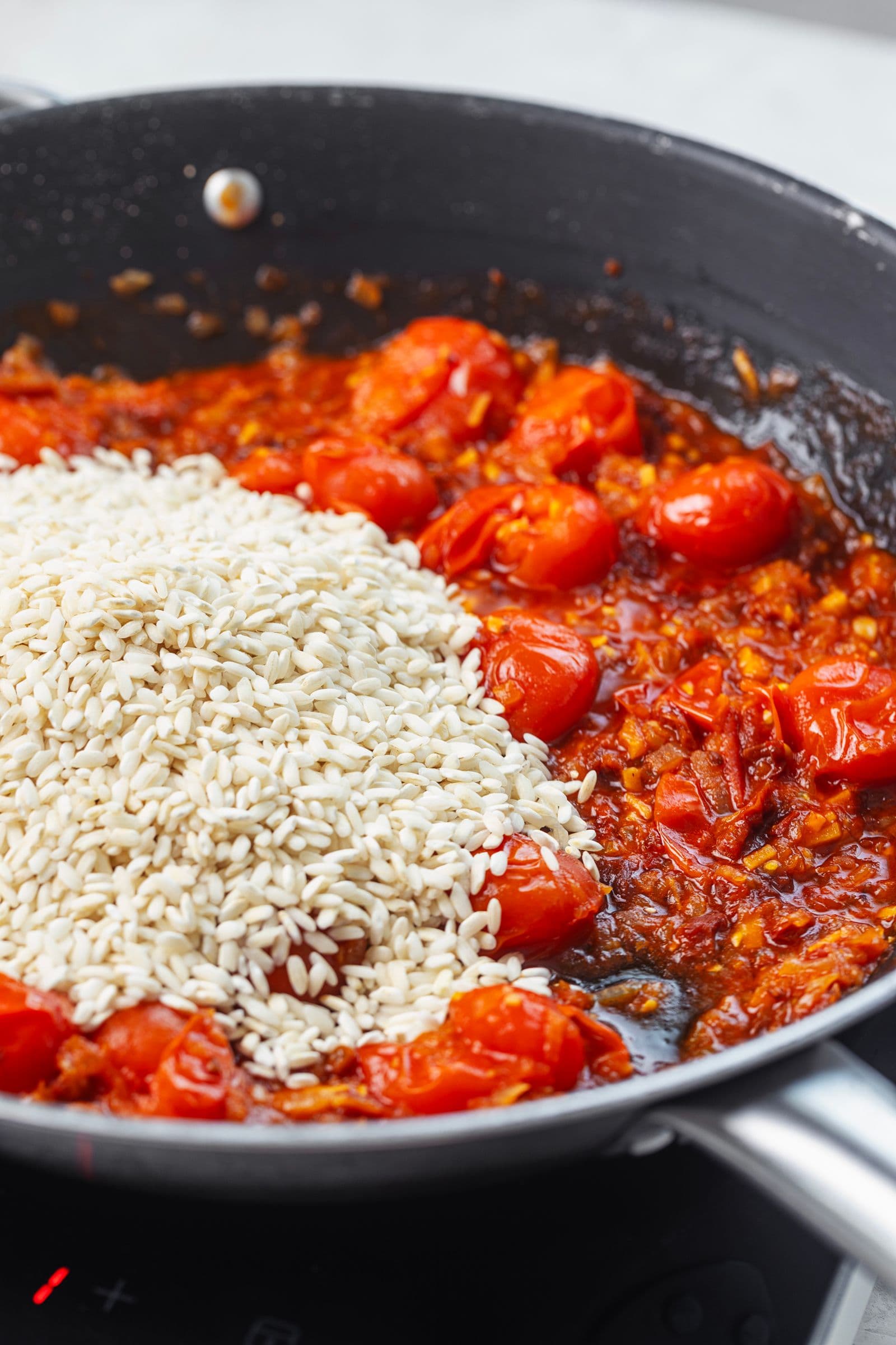 Arroz Carnaroli adicionado à mistura de tomate na frigideira, pronto a ser tostado antes de juntar o caldo.