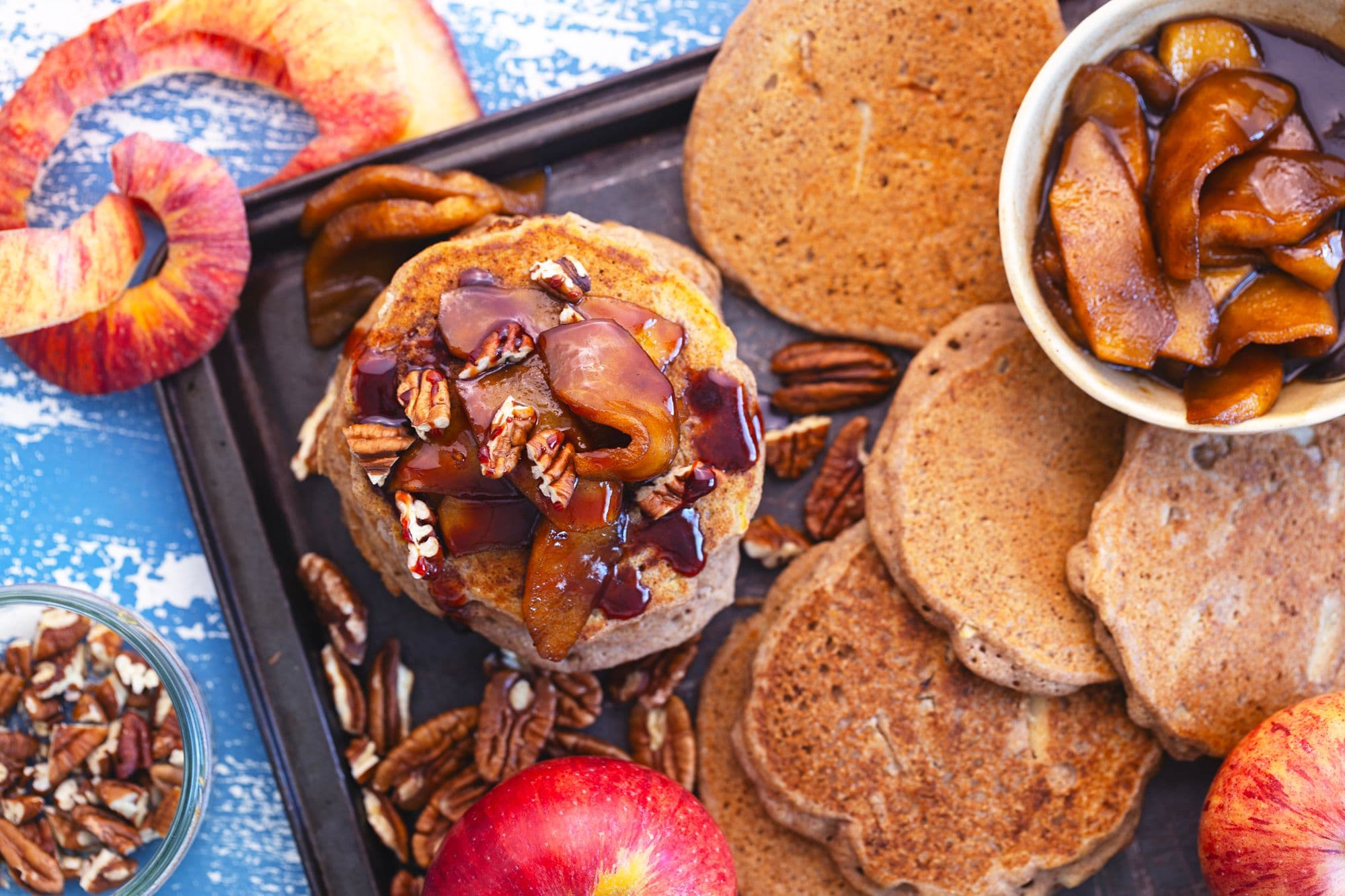 Overhead view of pancakes, apples, caramelised apple topping and pecans.