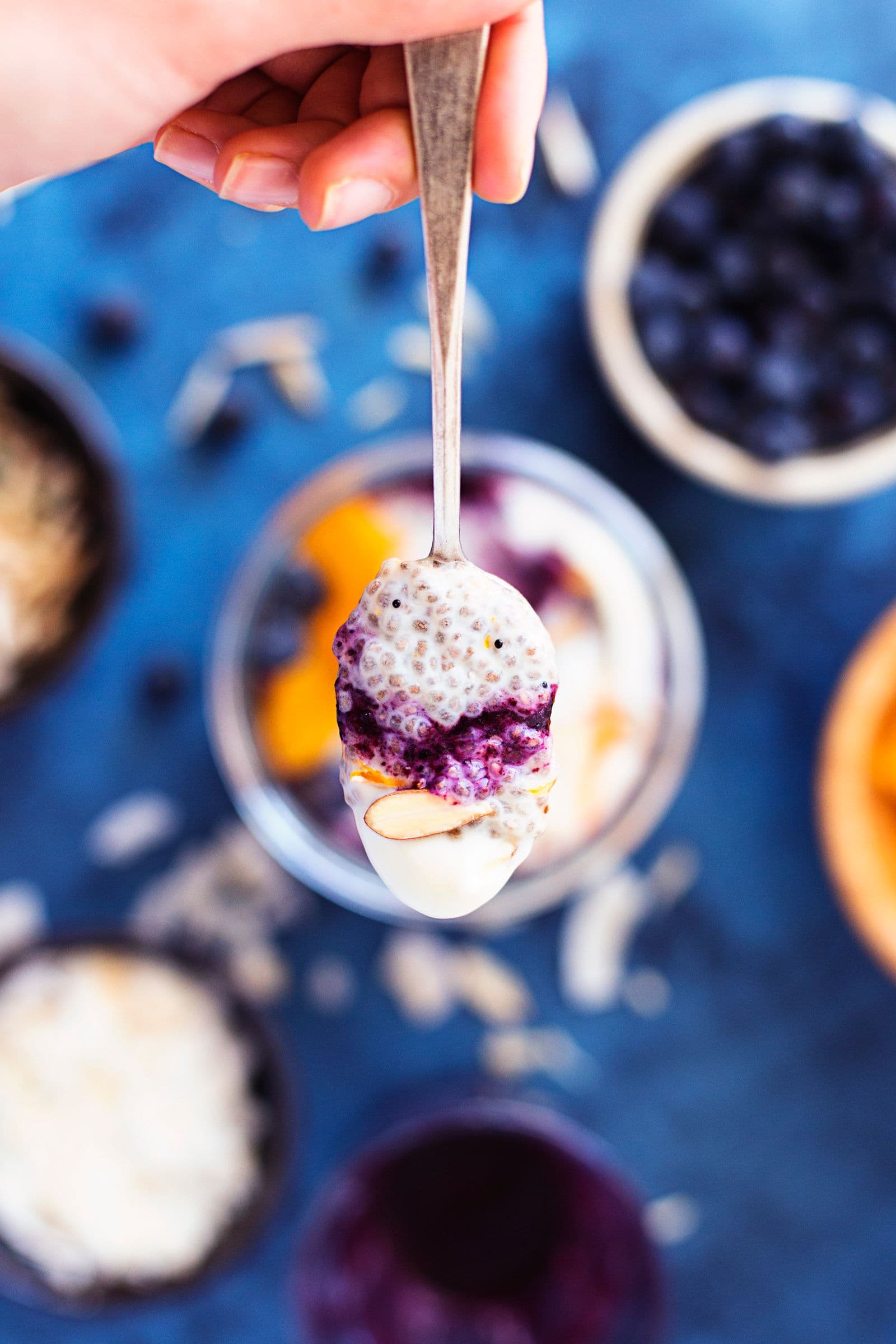 Hand holding a spoonful of chia pudding with blueberries and almond flakes above the jar.