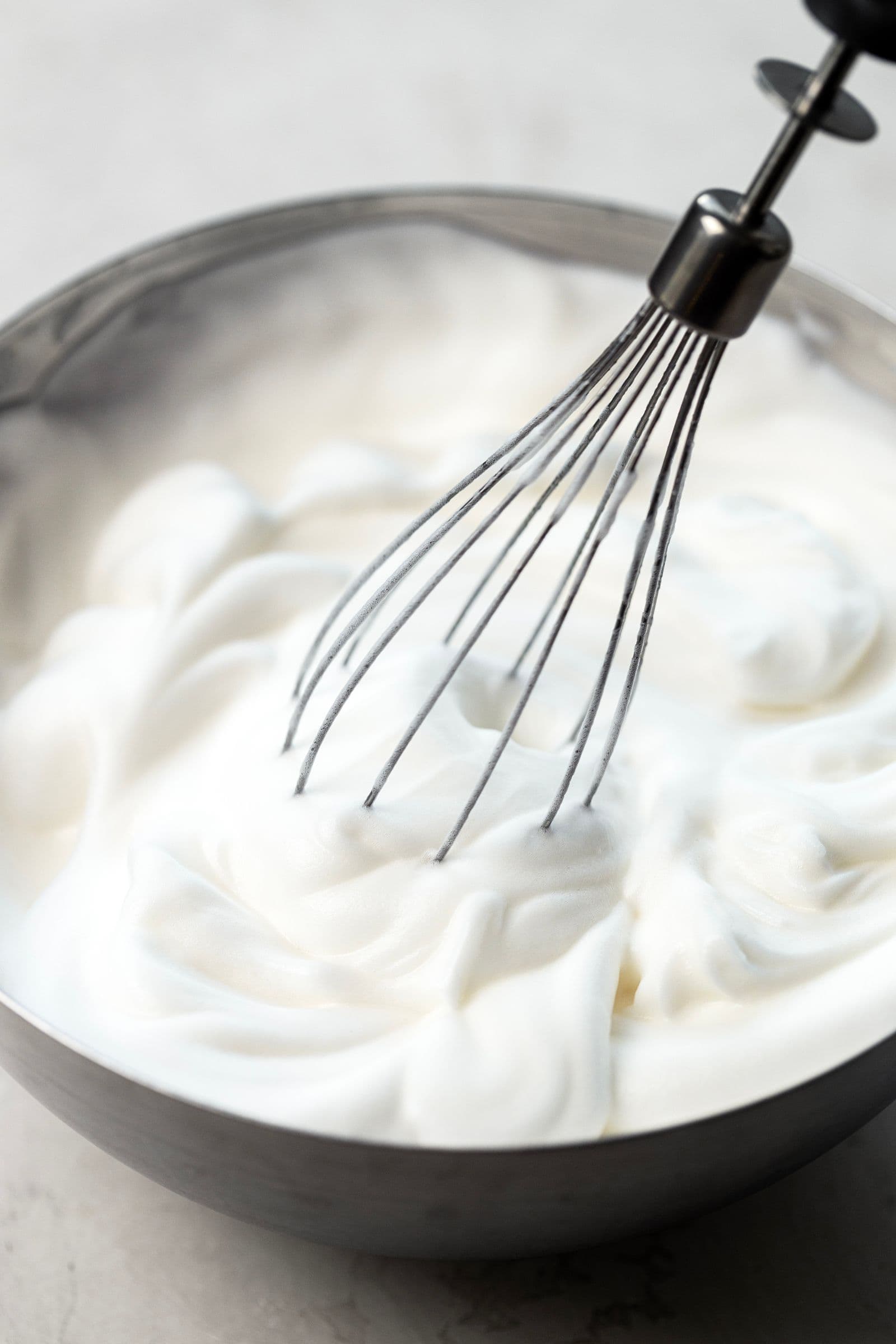 Aquafaba batida até ficar branca, fofa e volumosa, numa taça de inox.