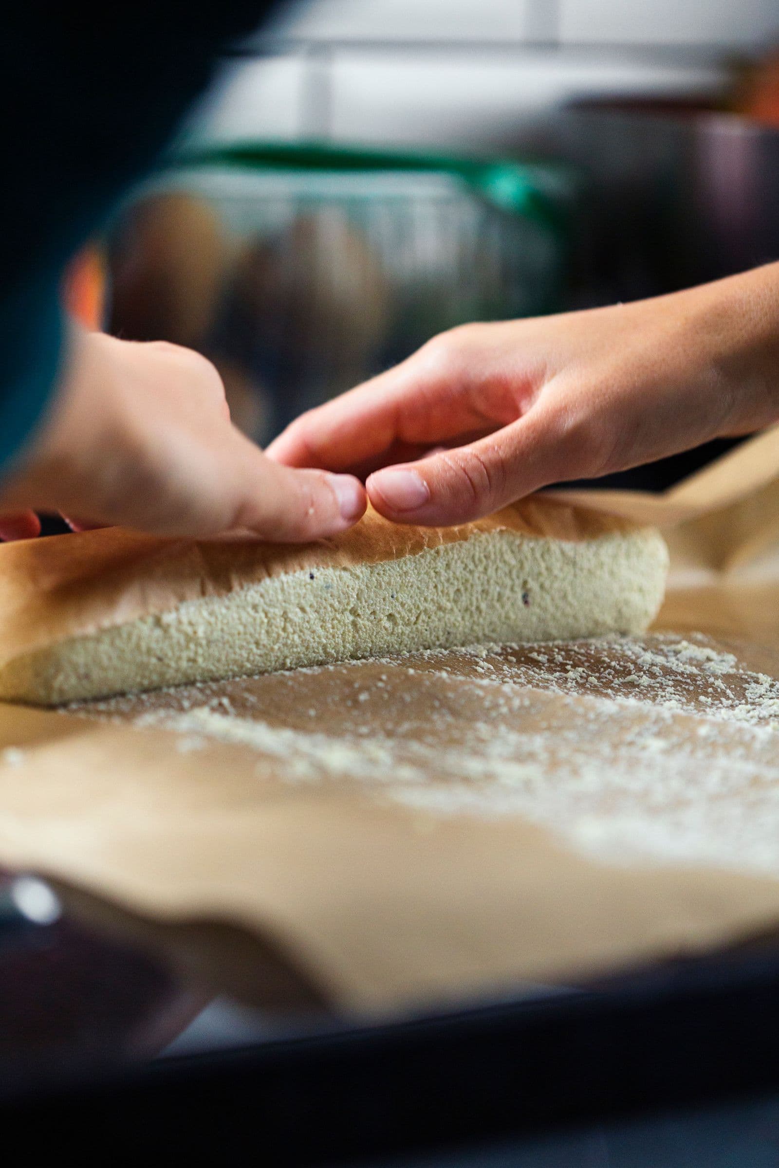 Mãos a moldar mistura de queijo de caju em formato de rolo sobre papel vegetal.