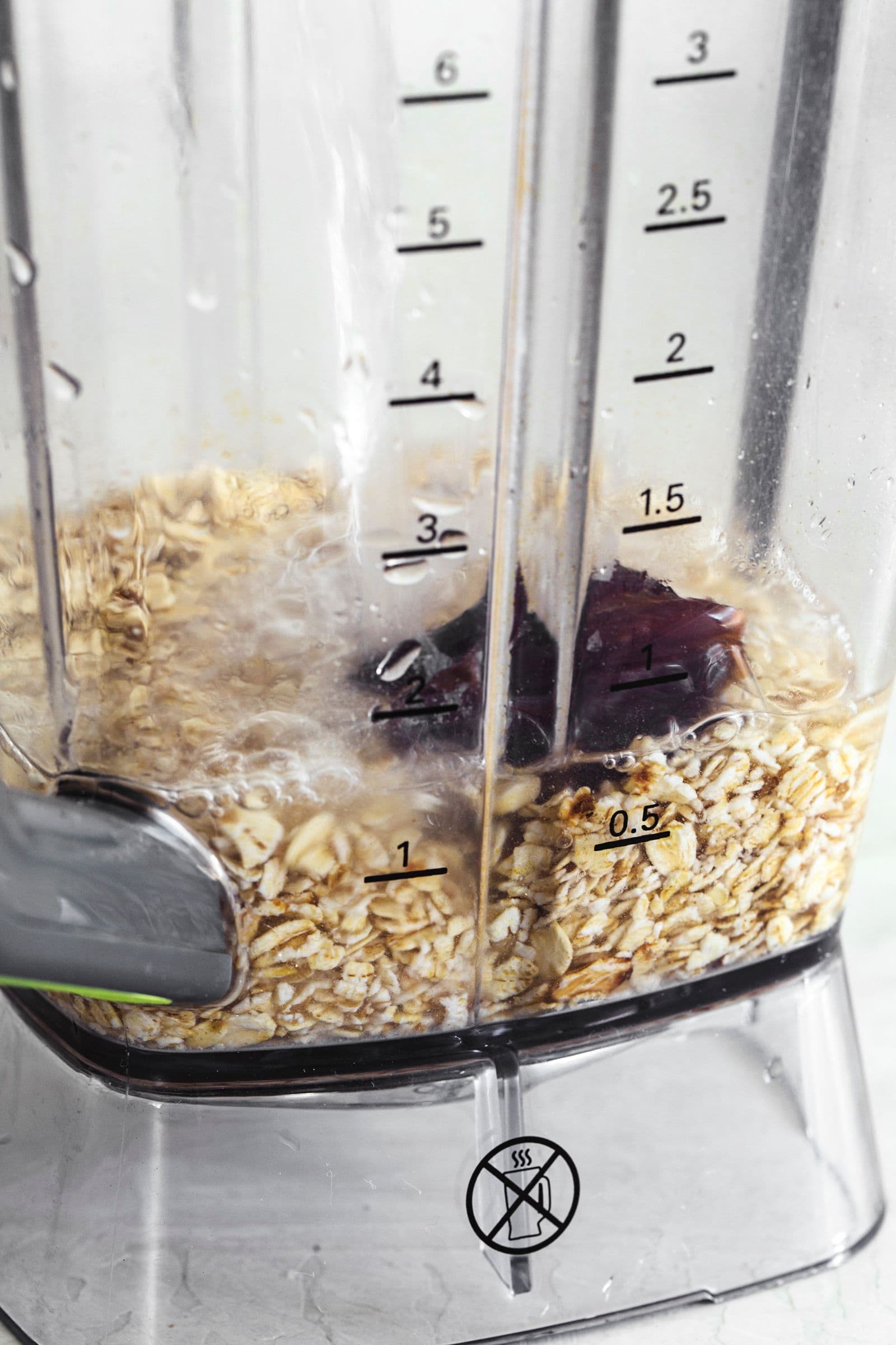Ingredients for homemade oat milk with a date inside a blender, partially covered with water.