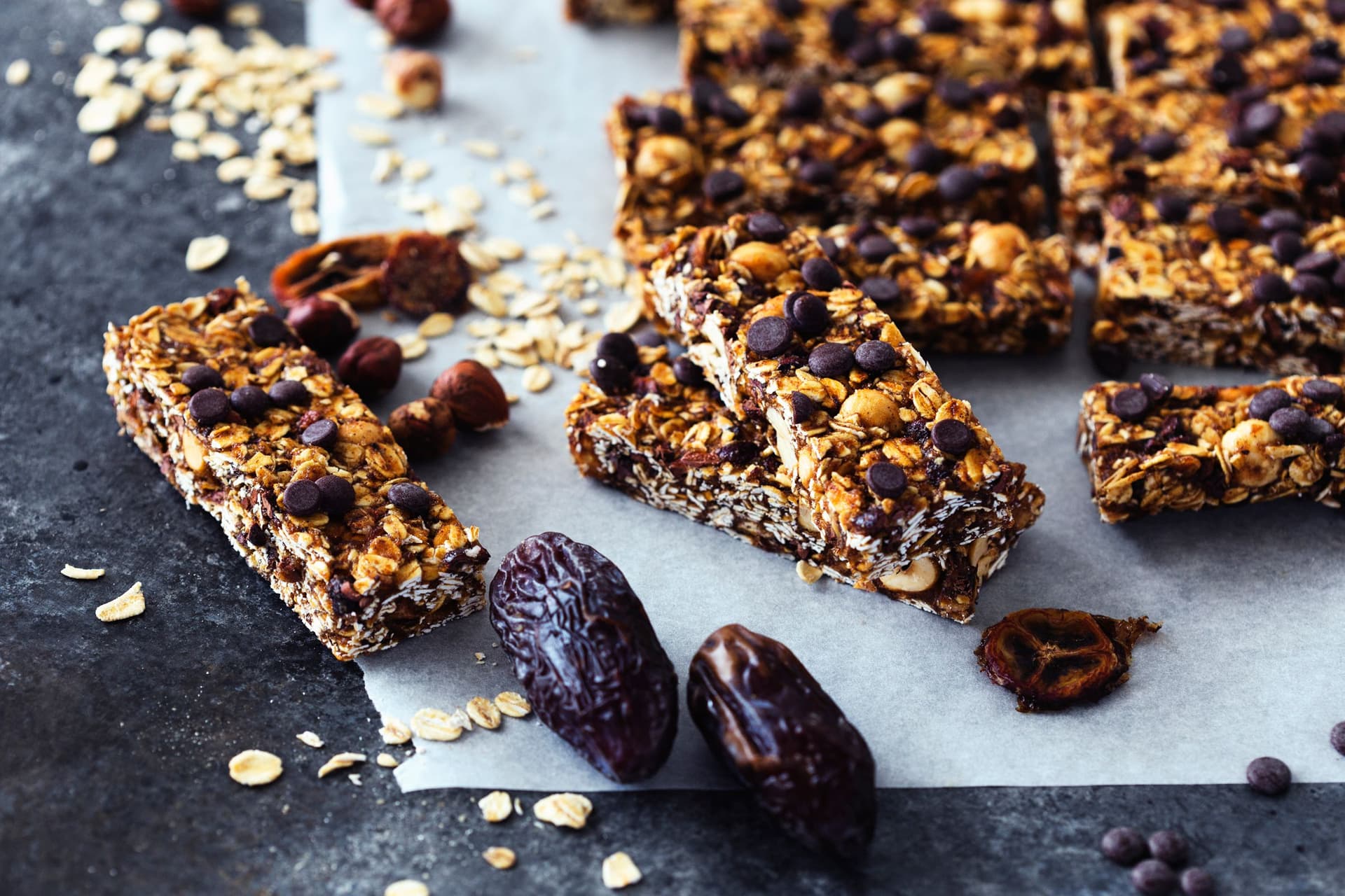 Barras de granola cortadas vistas de lado, com ingredientes espalhados em seu redor.