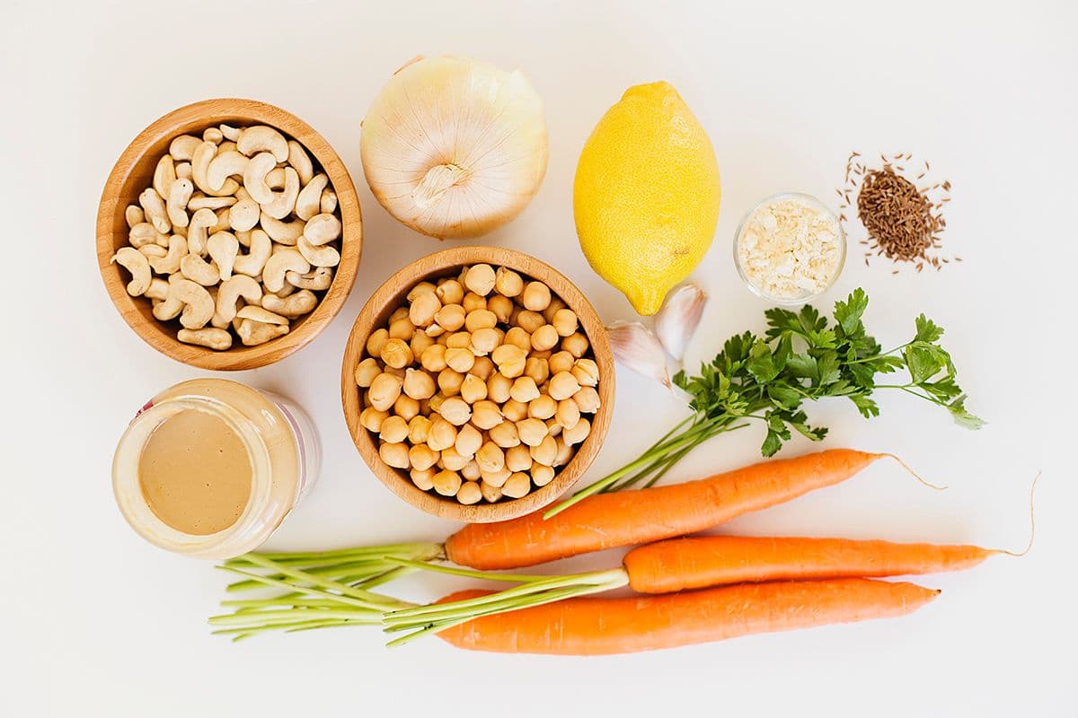 Carrot, lemon, cashews, chickpeas, herbs and spices on a light surface.