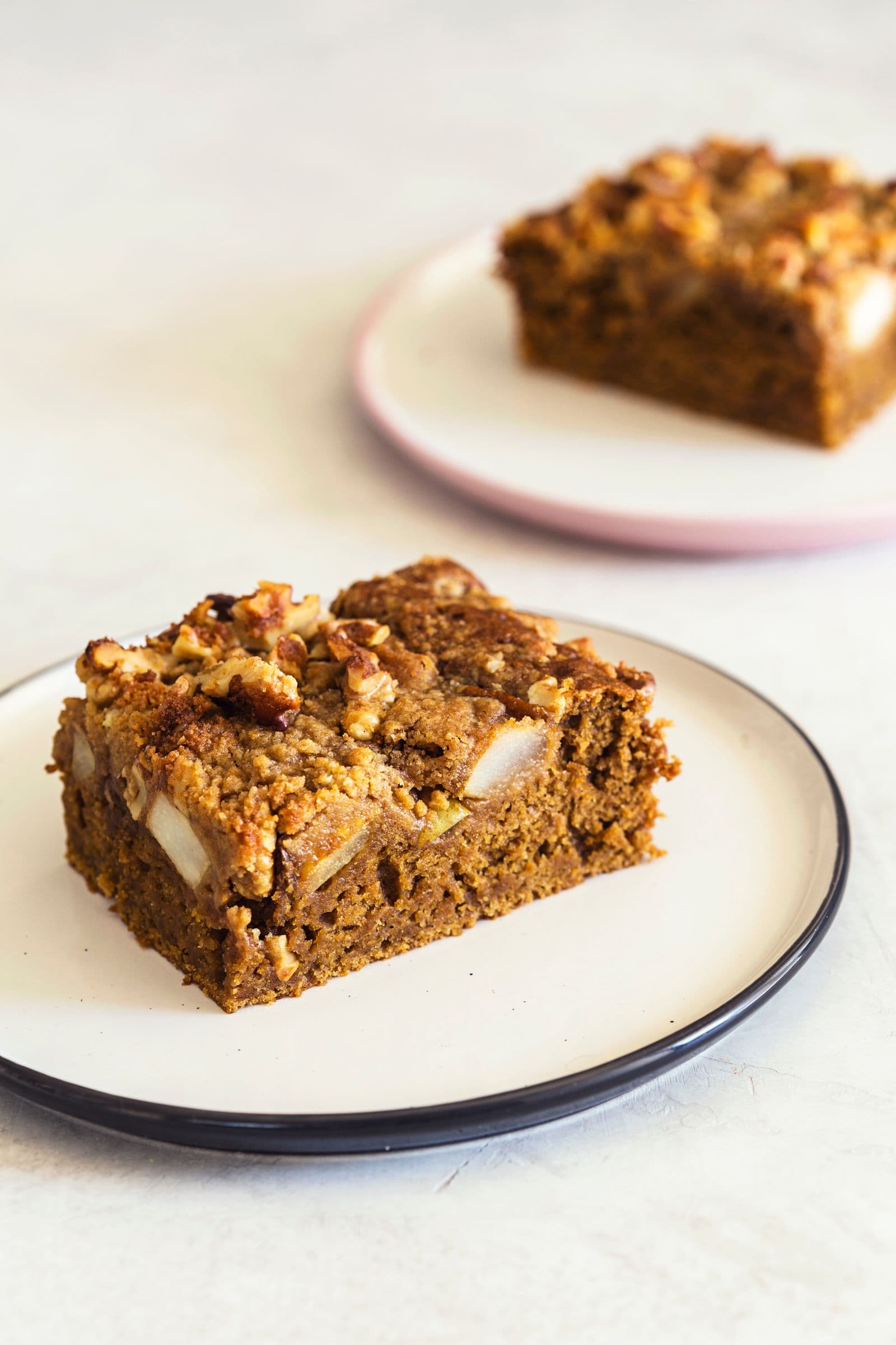 Uma fatia quadrada de bolo de café com pedaços de pêra visíveis num prato pequeno.
