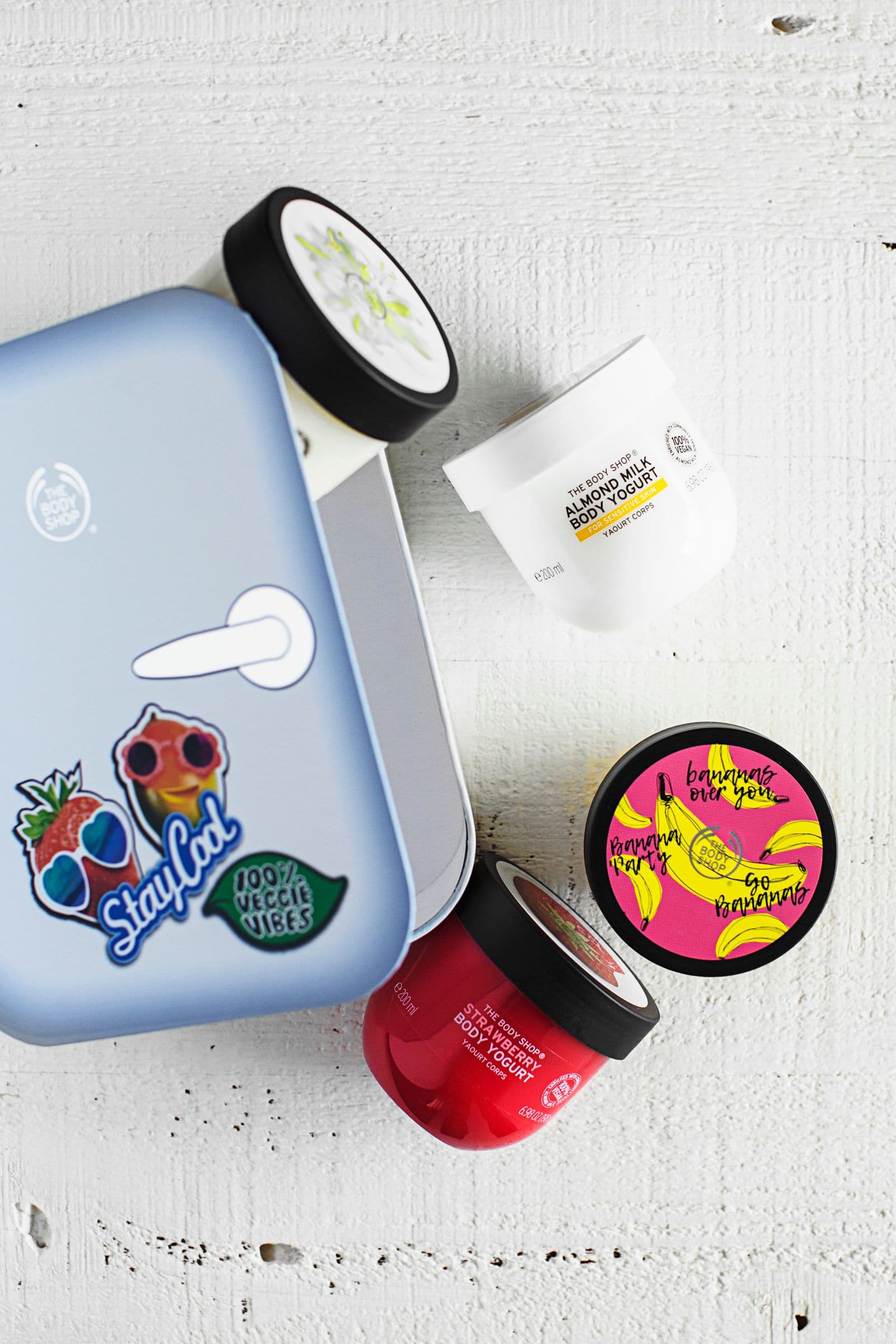Iogurtes corporais da The Body Shop dispostos sobre fundo branco ao lado de uma caixa temática.