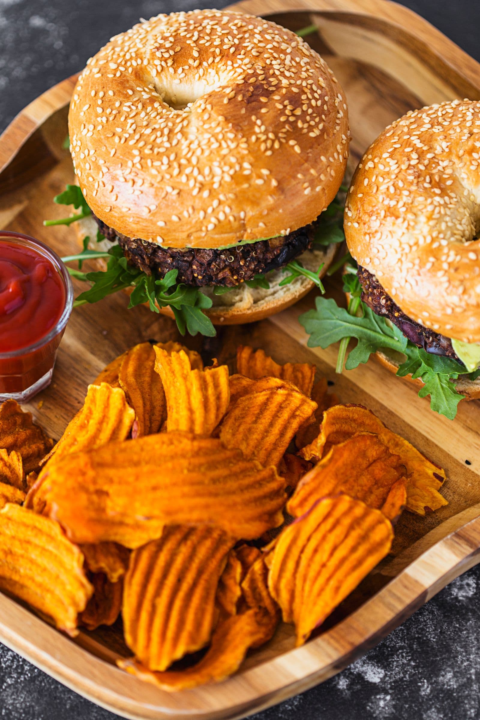 Overhead of two vegan burgers with sweet potato chips on a wooden plate.