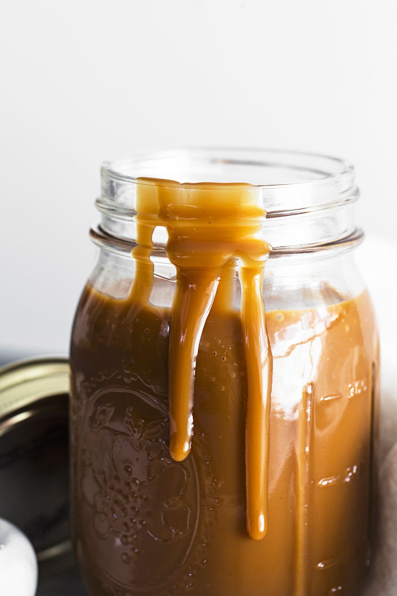 Glass jar with vegan coconut salted caramel dripping down the sides.