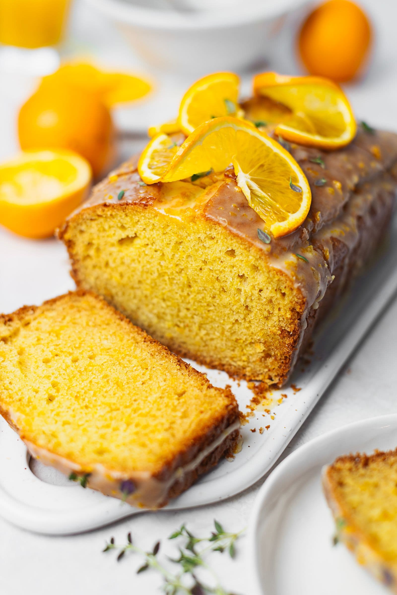 Bolo de laranja fatiado com calda, decorado com laranja e tomilho, com uma textura fofa e dourada.