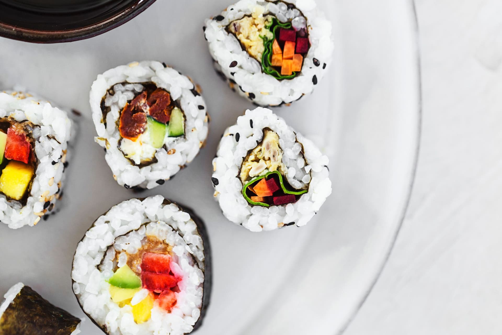 Foto aproximada de vários rolinhos de sushi vegan com recheios coloridos de legumes.