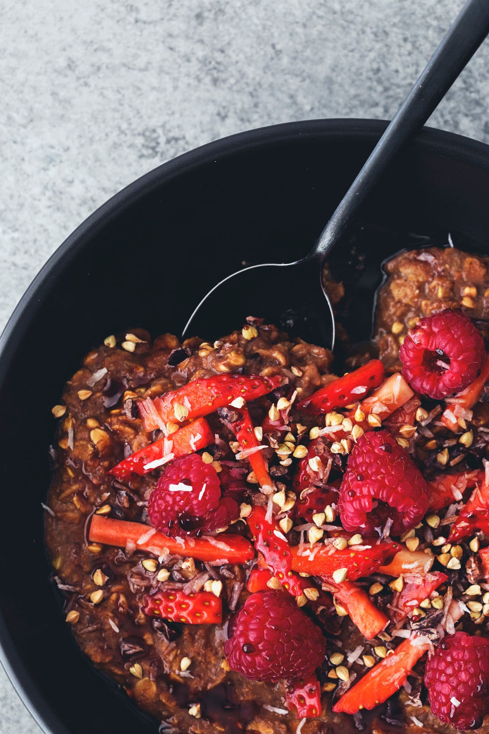 Spoon lifting a bite of cacao oatmeal with raspberries and strawberries from the bowl.