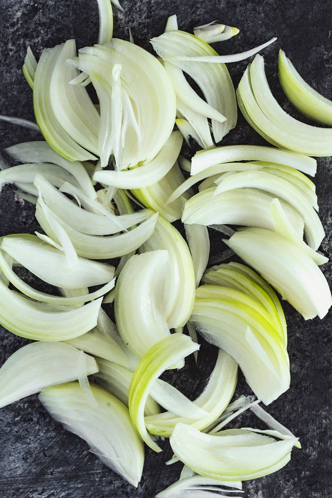 Cebolas frescas cortadas finamente sobre fundo escuro, prontas a cozinhar.