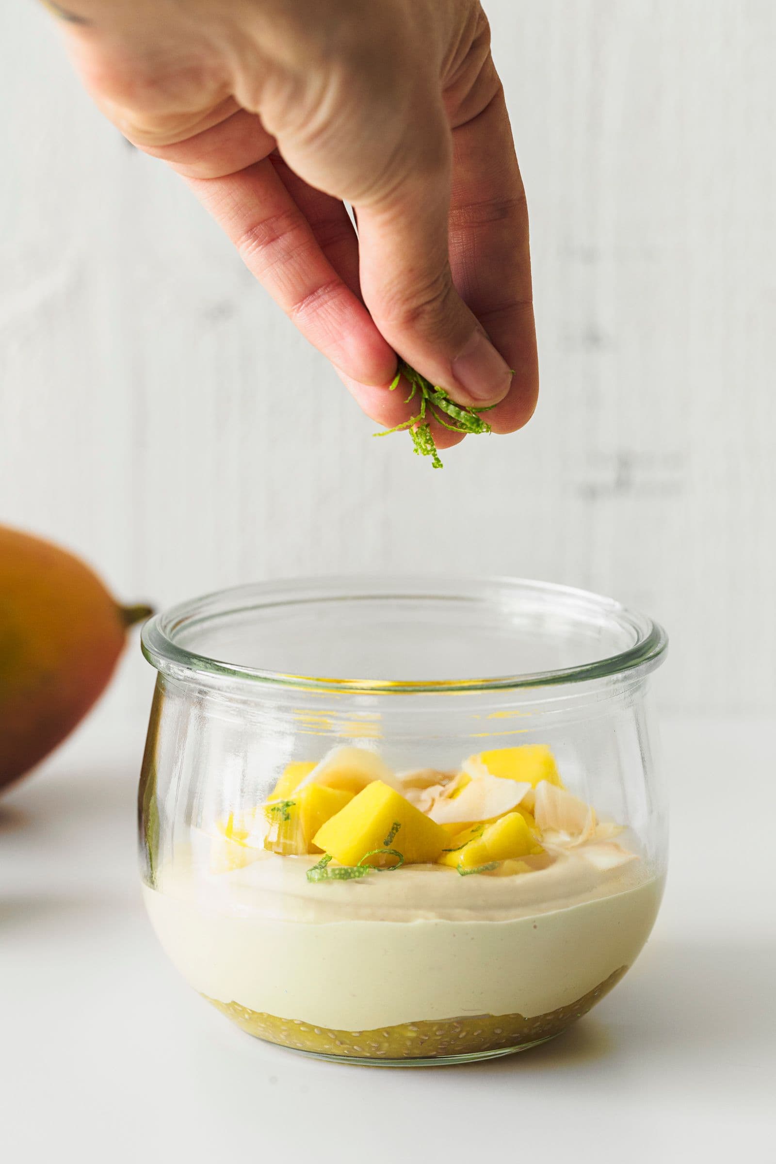 Hand sprinkling lime zest over a freshly made mango cashew yogurt jar.