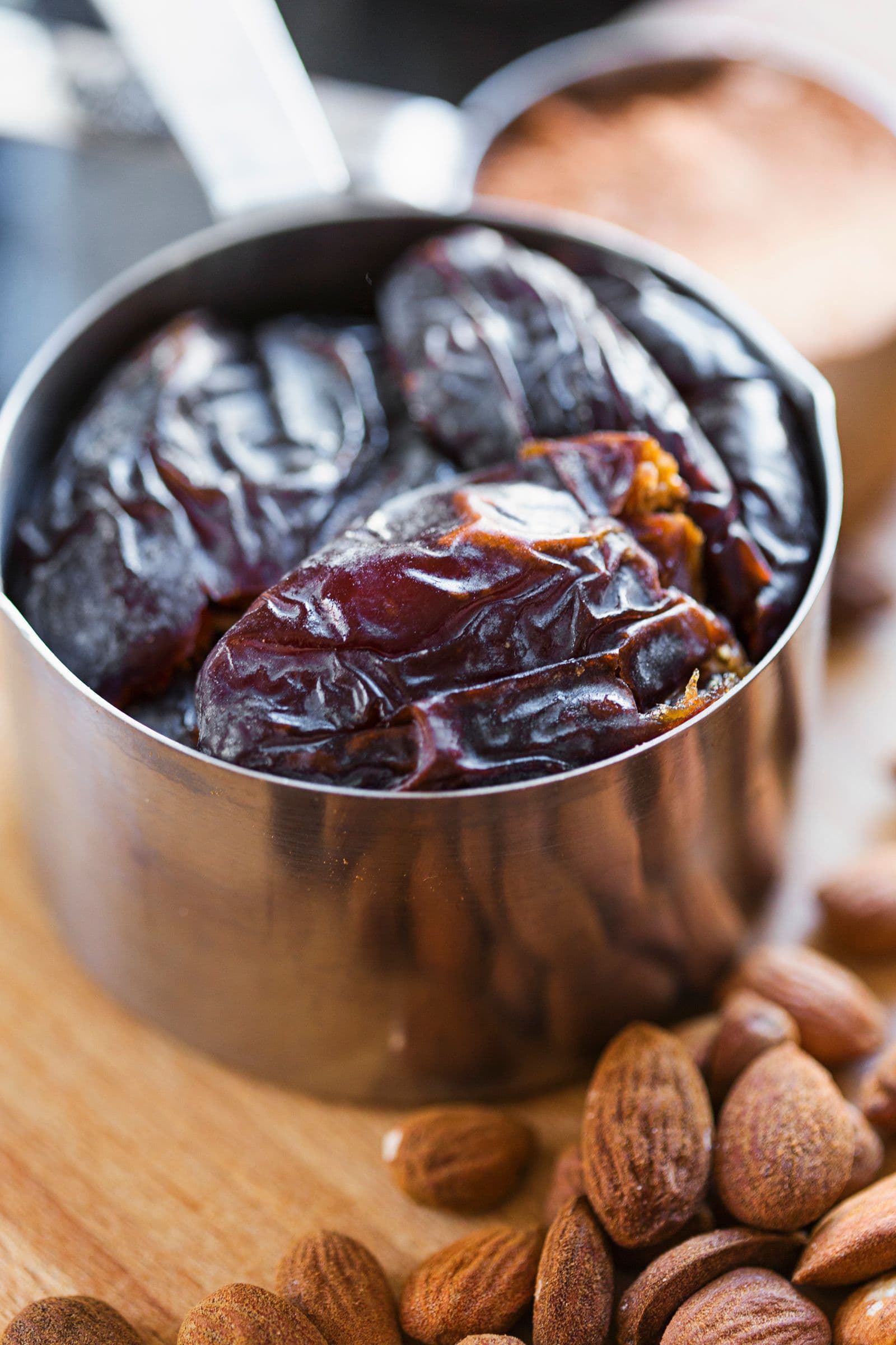 Medjoul dates in a metal cup with almonds and cocoa in the background.