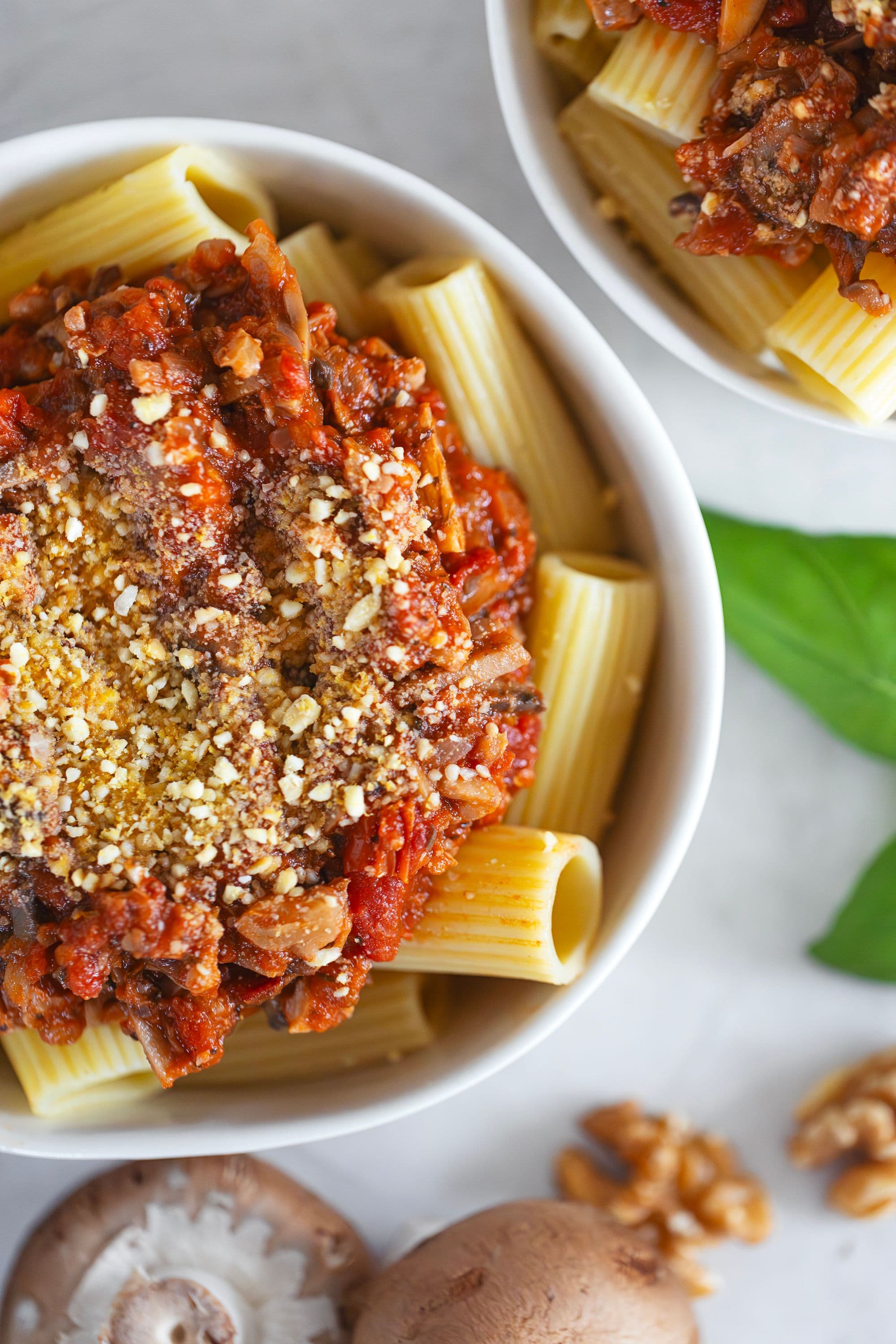 Close-up of pasta bowl with spicy walnut bolognese and a basil leaf.