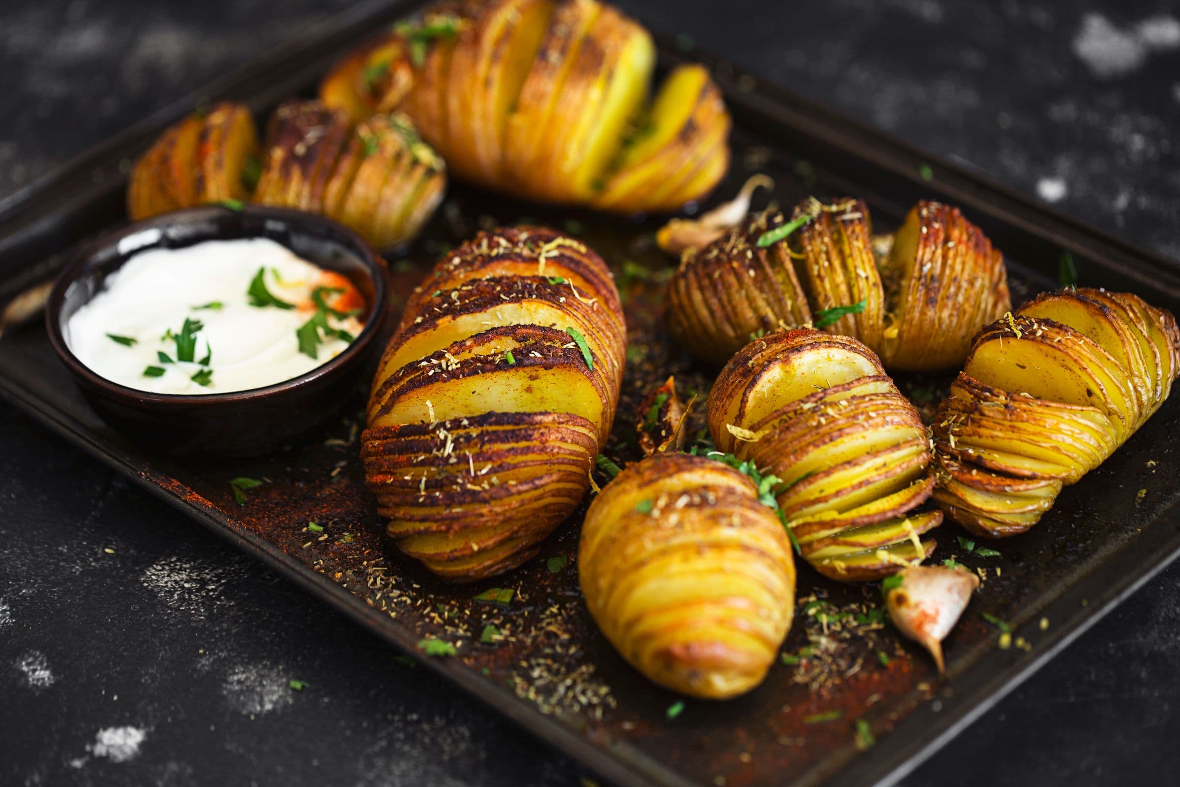 Baking tray with beautifully baked Hasselback potatoes and a ramekin of plant-based mayo.