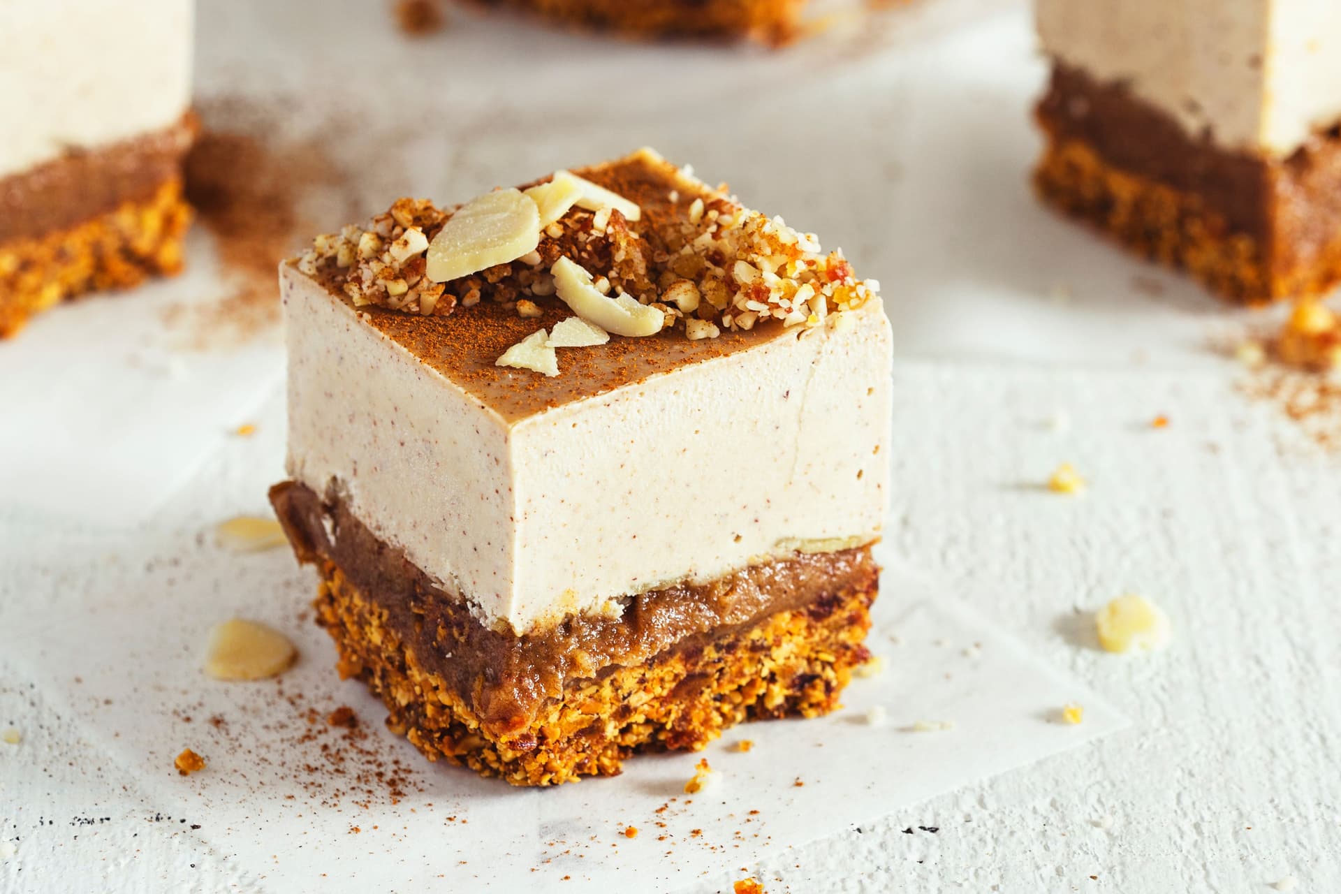 Fatia individual de cheesecake vegan em camadas com cobertura de caramelo e amêndoas.