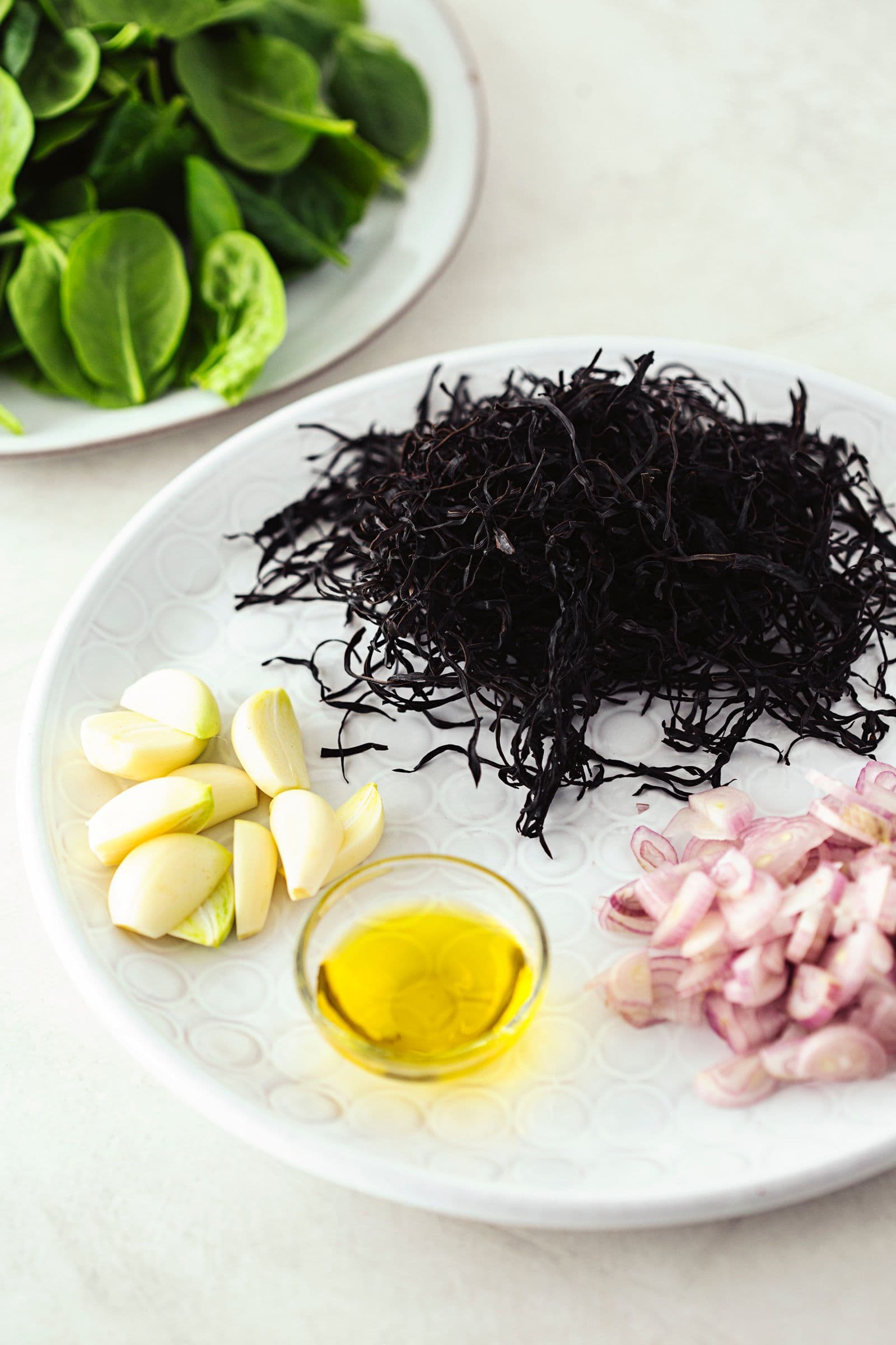 Fresh spinach, arame seaweed, garlic cloves and chopped shallots with olive oil on a plate.