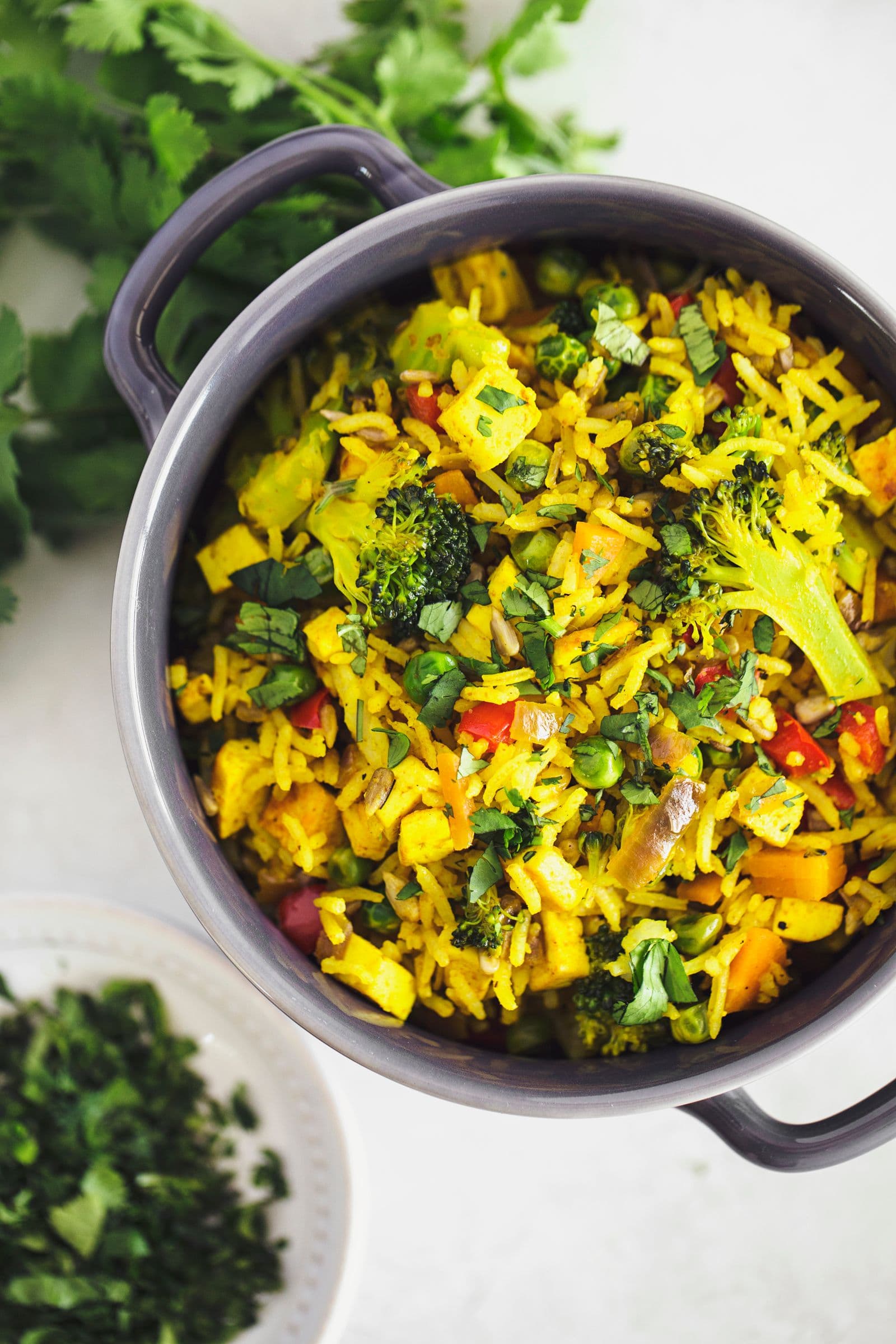 Cerâmica cinzenta com arroz frito vegan guarnecido com coentros frescos, servido sobre mesa branca.