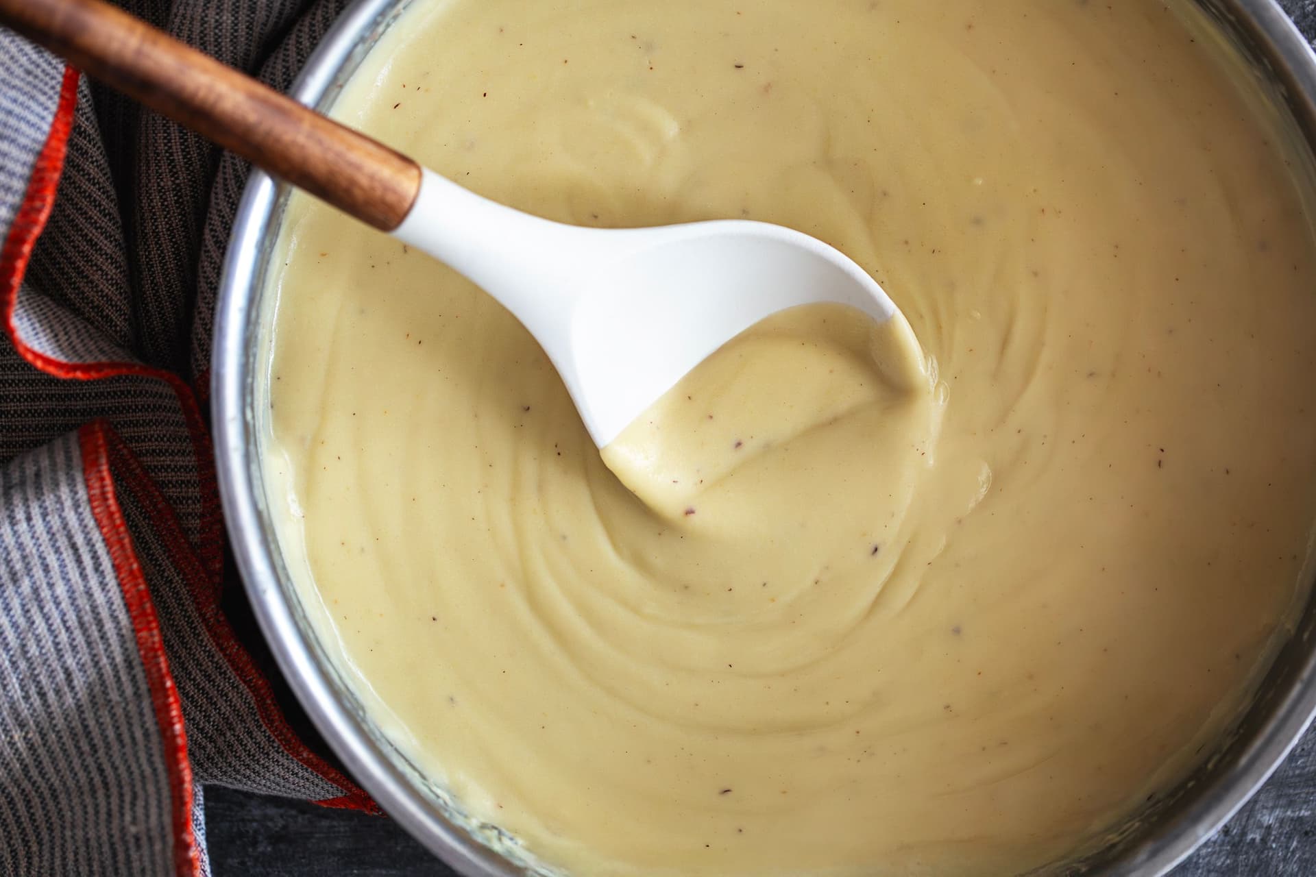Panela com molho béchamel cremoso, mexido com colher de cabo em madeira, pronto a servir