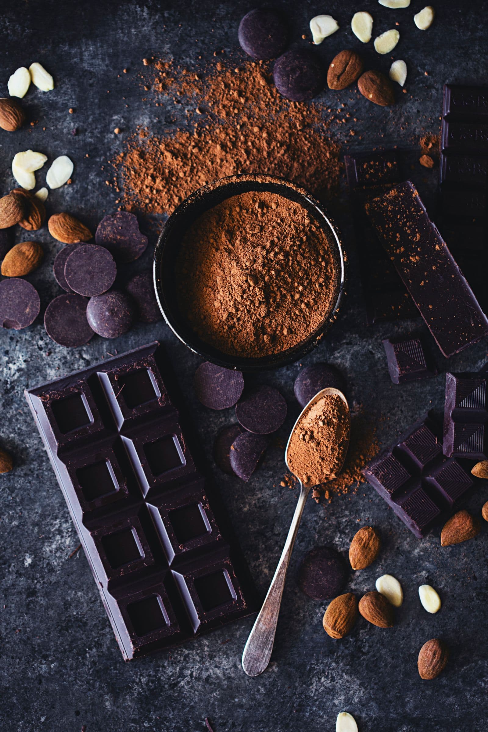 Flatlay of cocoa powder, almonds, chocolate pieces and almonds.