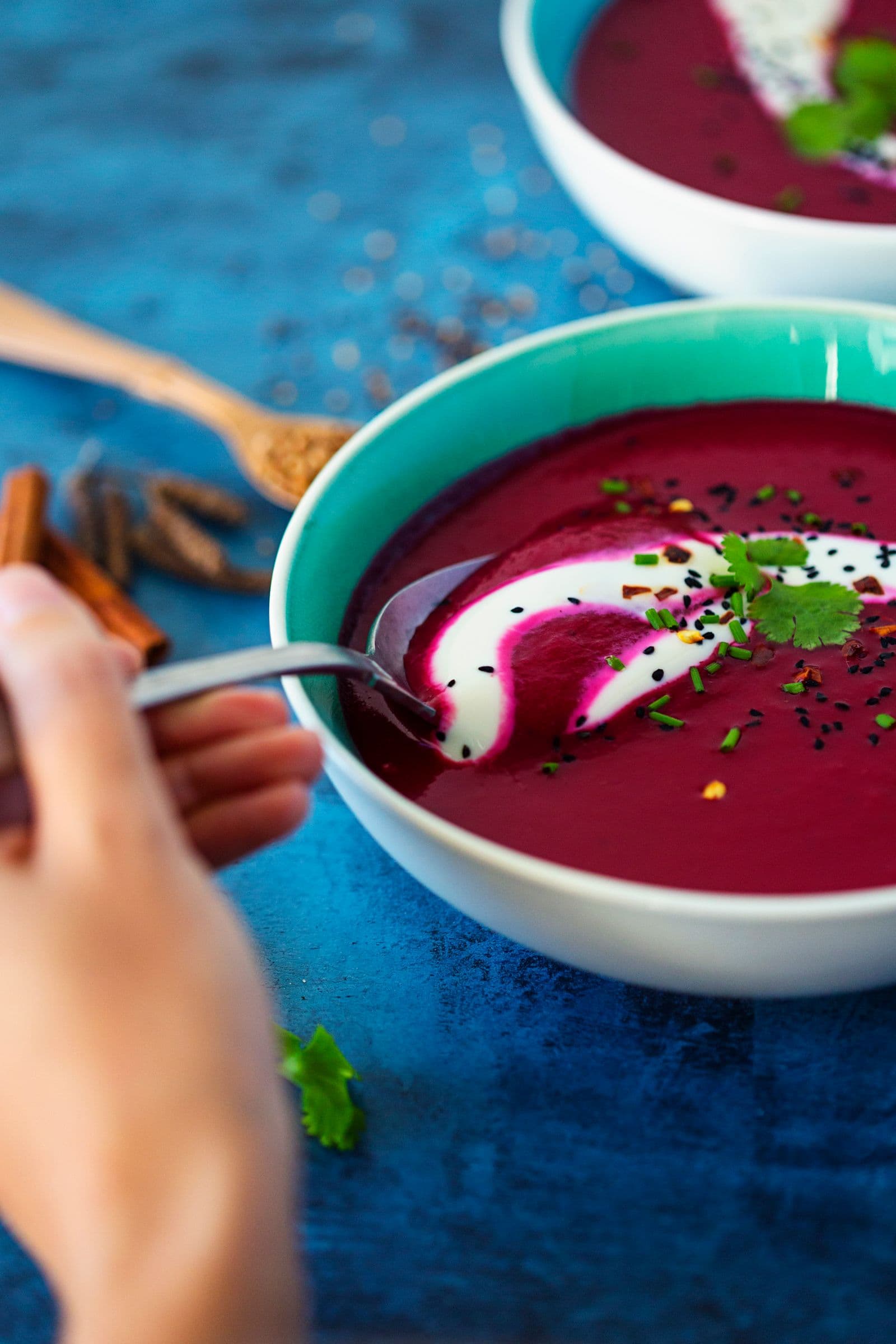 Spoon being dipped into vibrant beetroot soup with yogurt and fresh herbs.