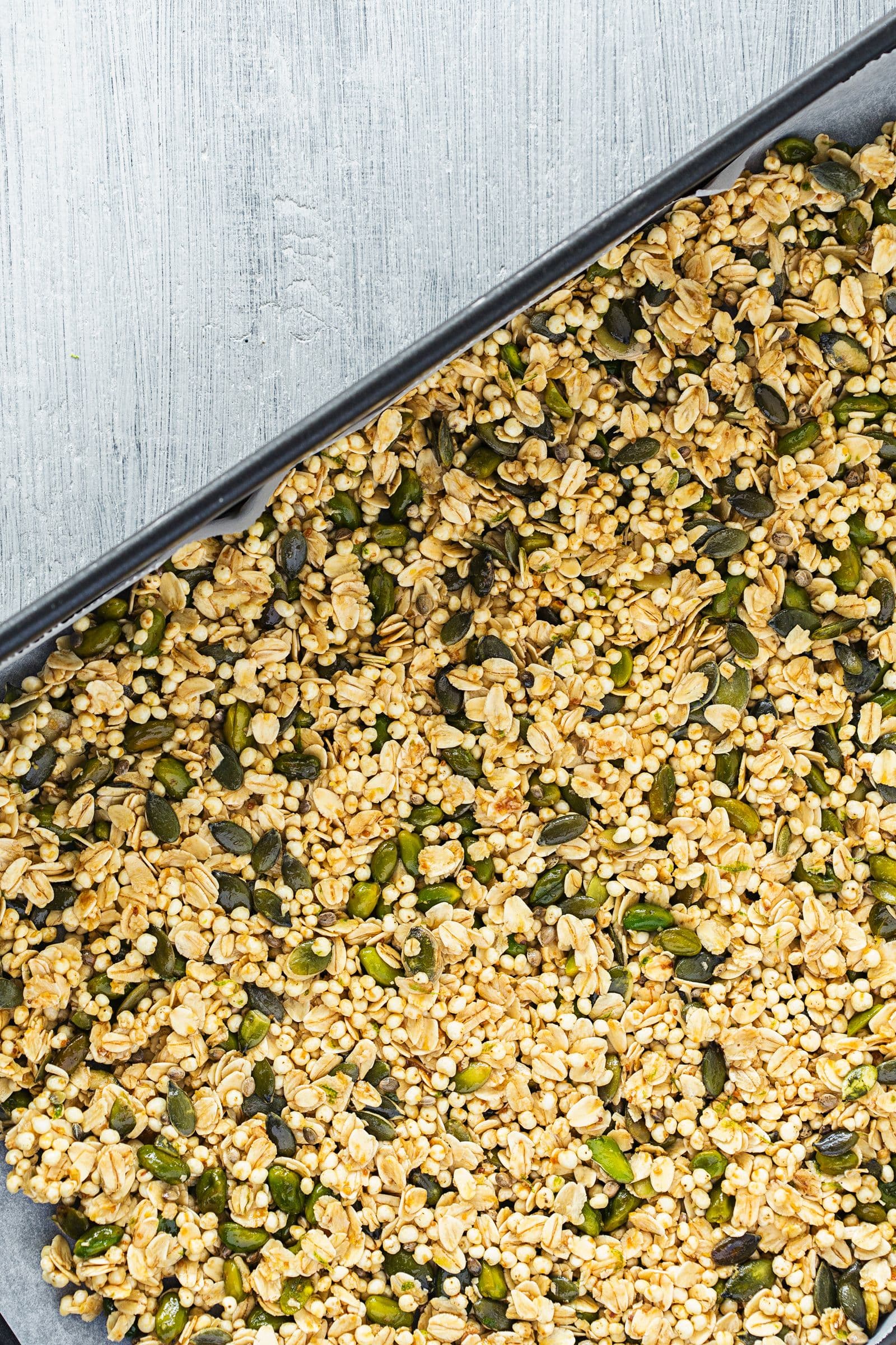 Granola verde crua distribuída num tabuleiro forrado com papel vegetal antes de ir ao forno.