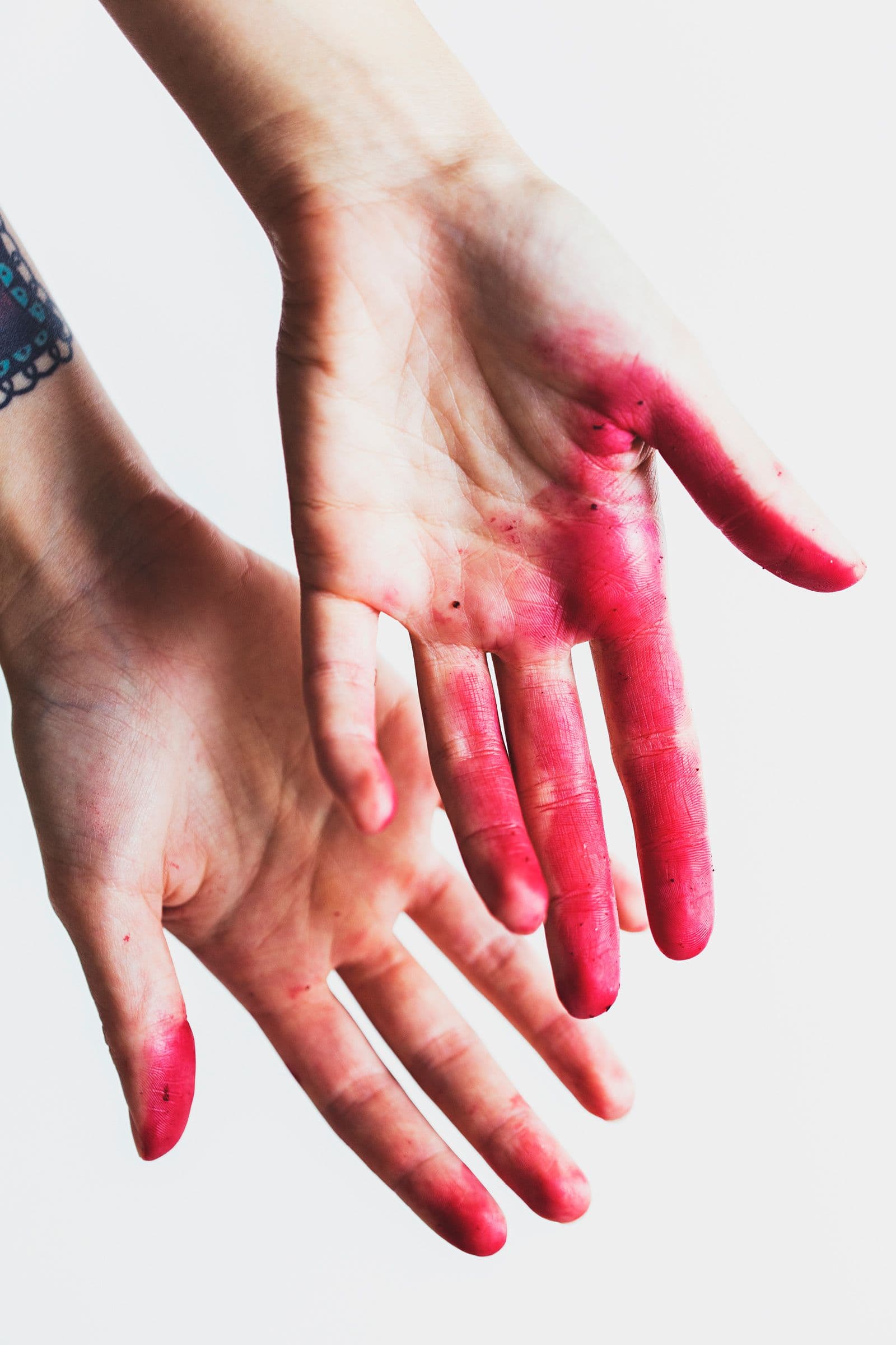 Hands stained bright pink from handling fresh beetroot.