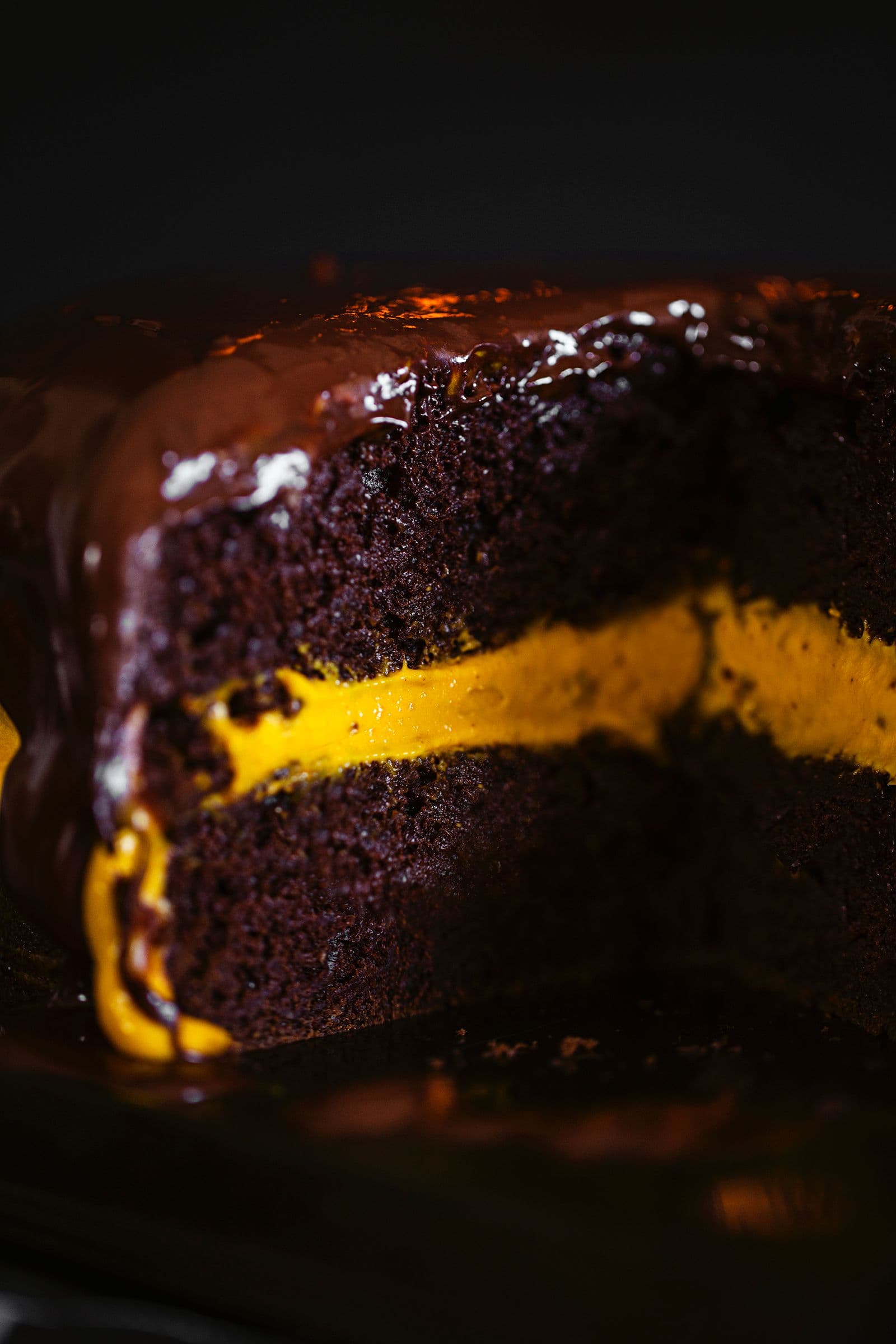 Close-up of a moist chocolate cake with orange creamy filling and shiny chocolate glaze on top.