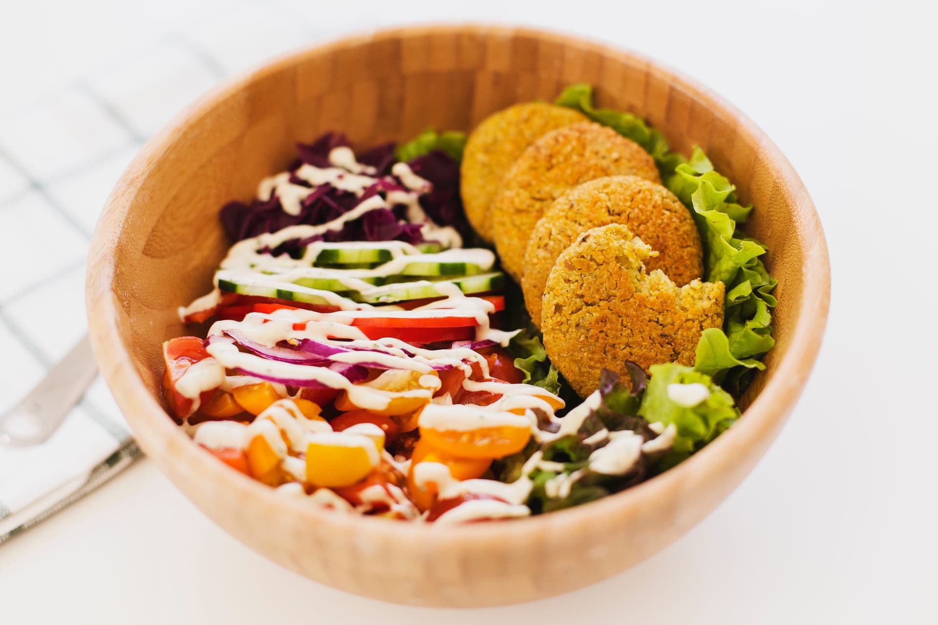 Taça com falafel, alface, legumes coloridos e molho cremoso de tahini.