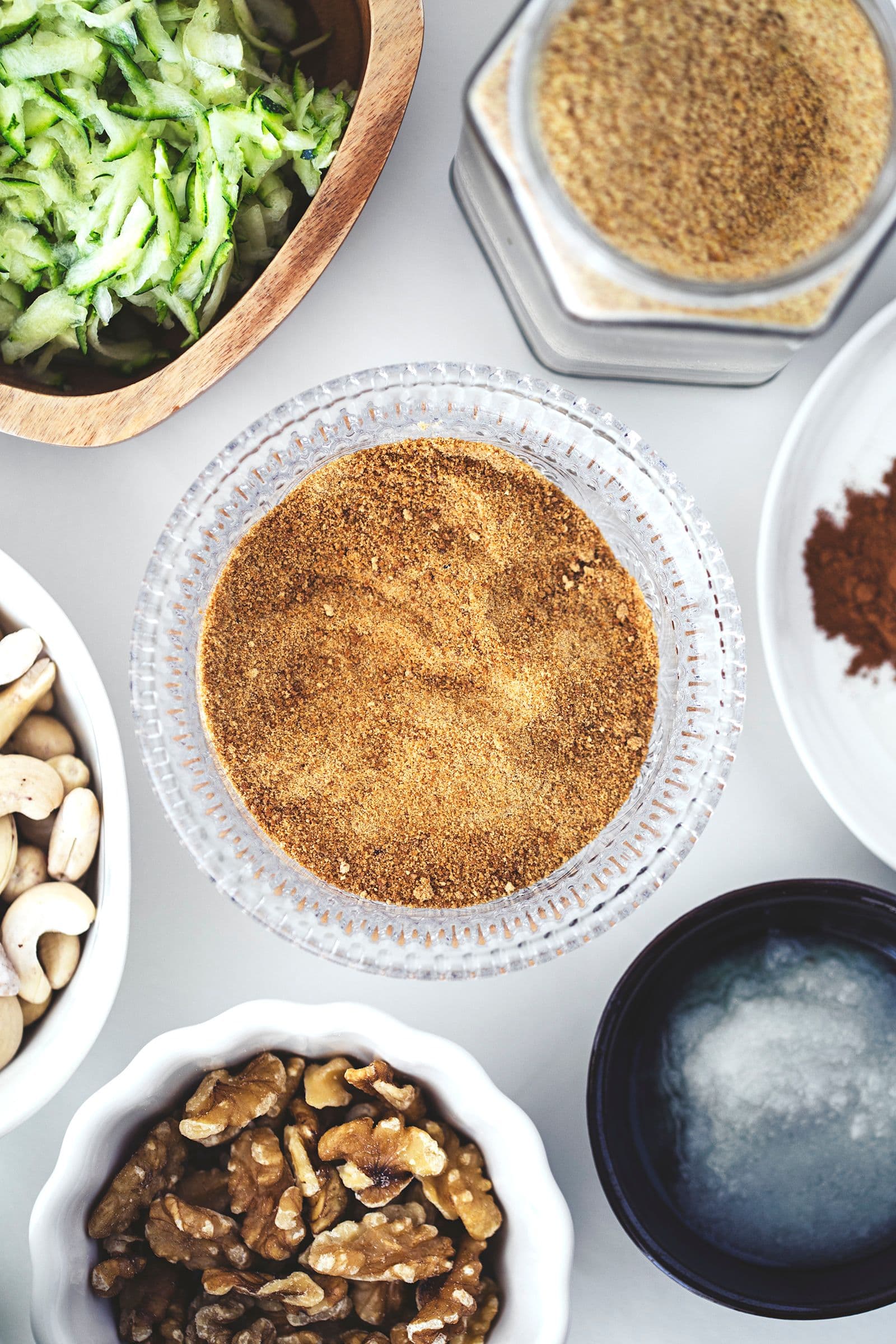 Todos os ingredientes secos e húmidos para o bolo de curgete e limão dispostos em taças pequenas.